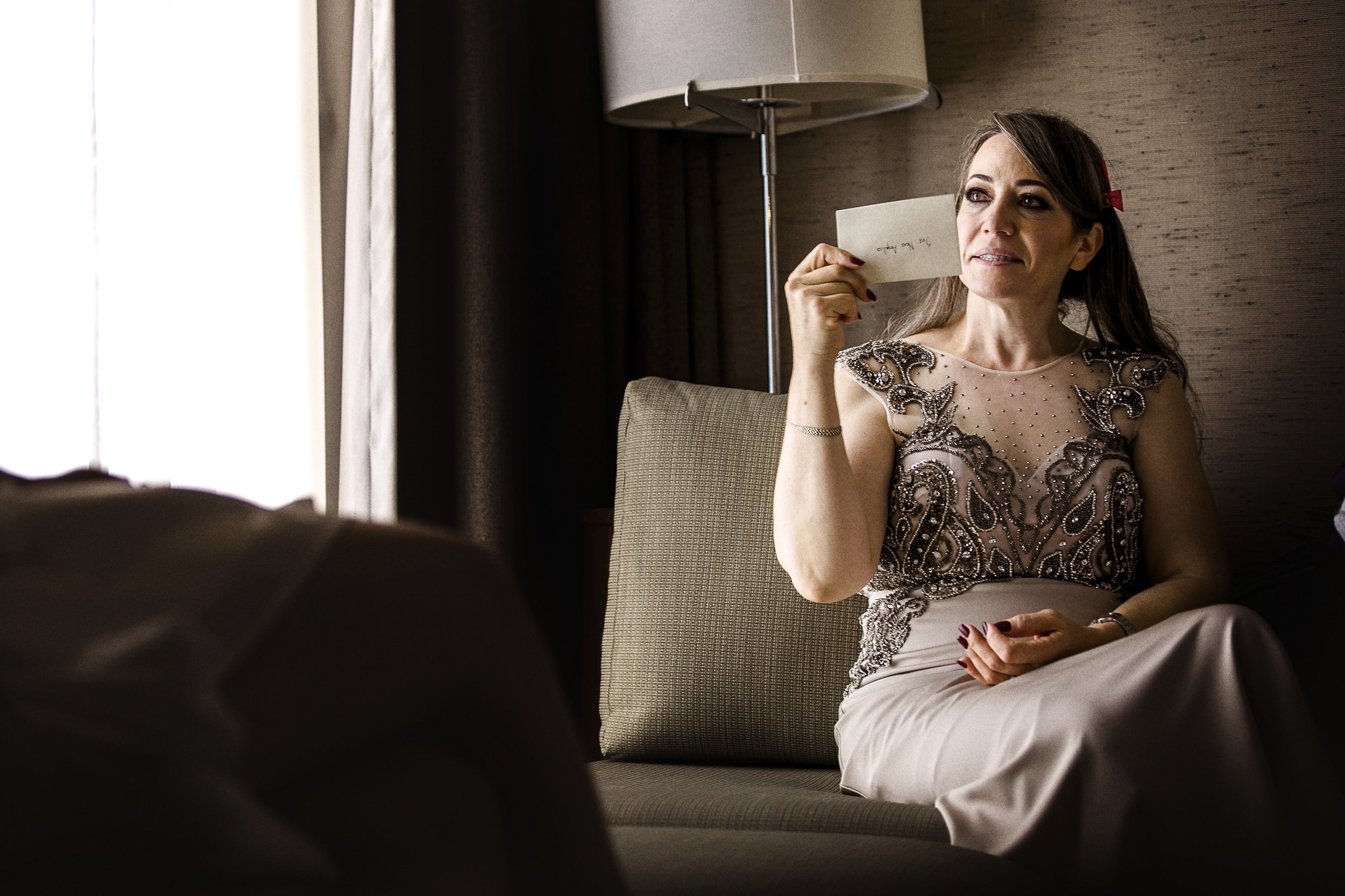 Fotografía documental de mujer sentada en sillón sosteniendo objeto, pausa durante la preparación.