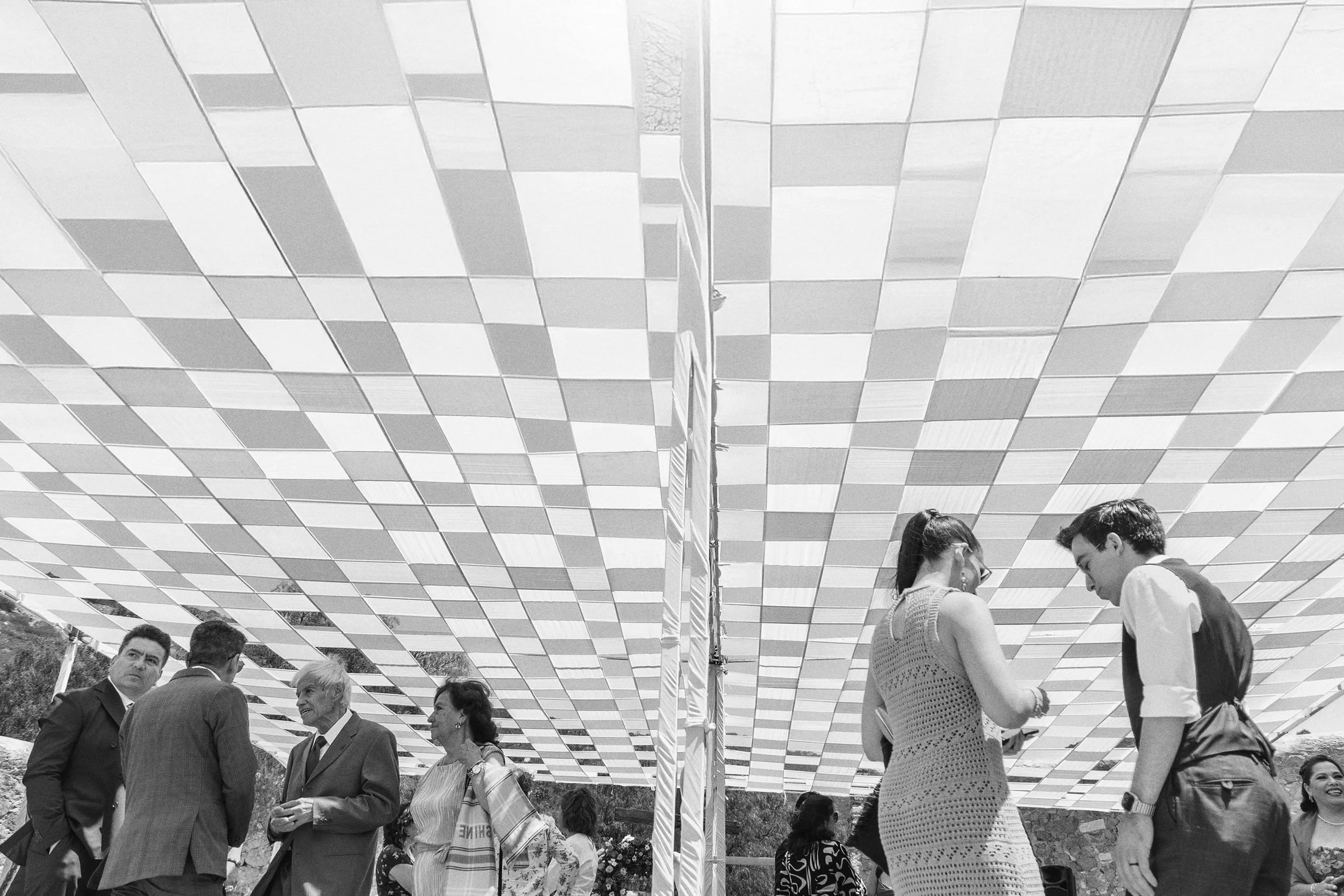 Fotografía documental en blanco y negro de invitados caminando bajo techo decorado.