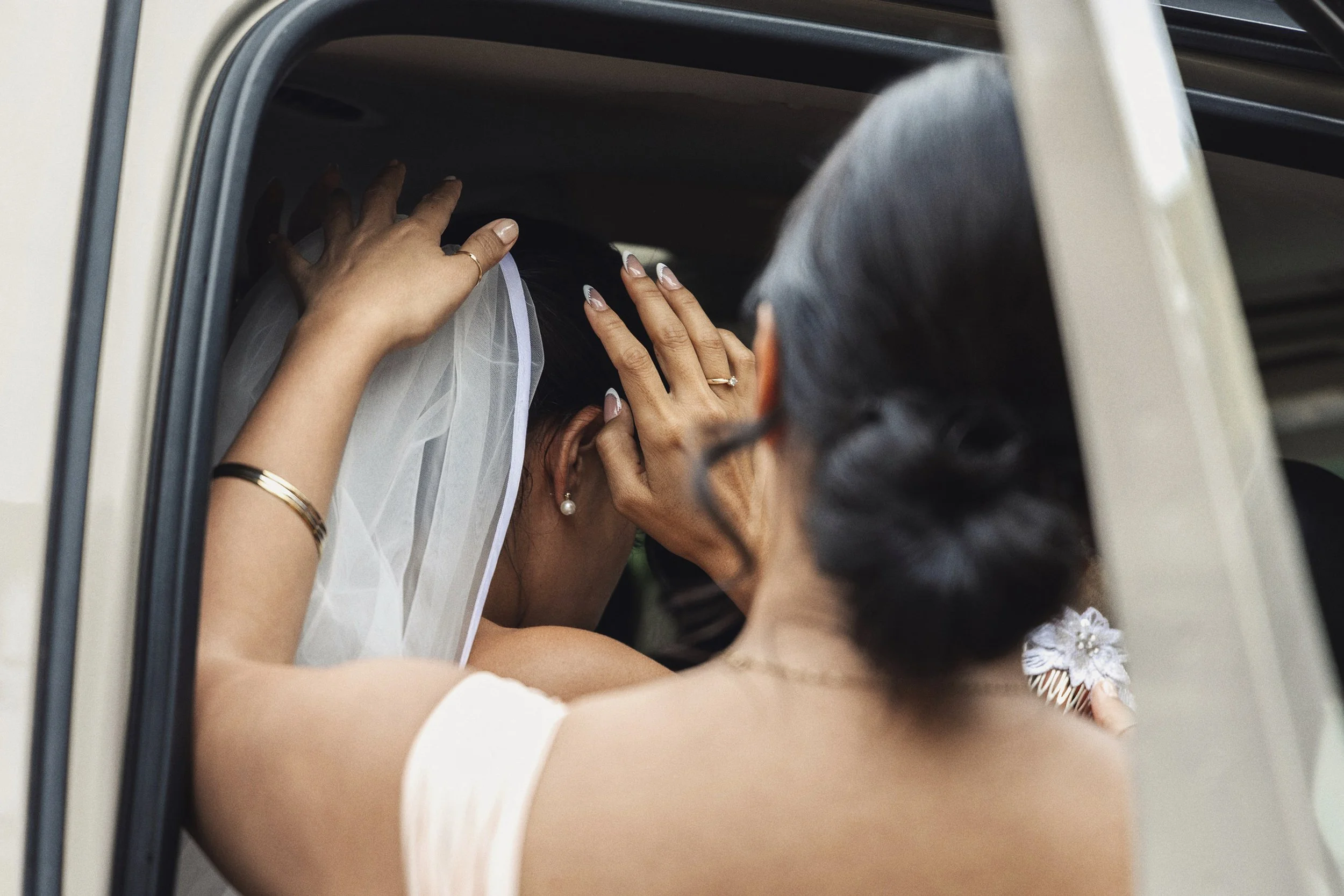 Fotografía documental de novia vista desde atrás dentro de un automóvil, manos levantadas ajustando velo.
