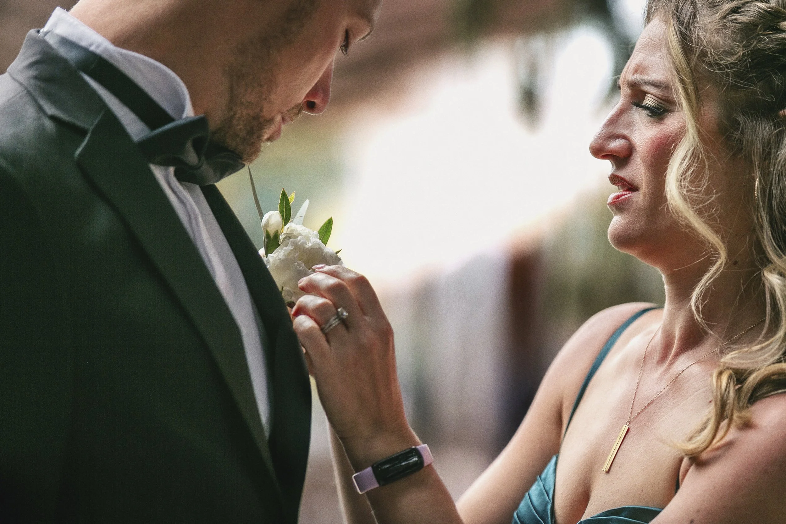 Fotografía documental de novios en primer plano, ajuste de boutonniere antes de la ceremonia.