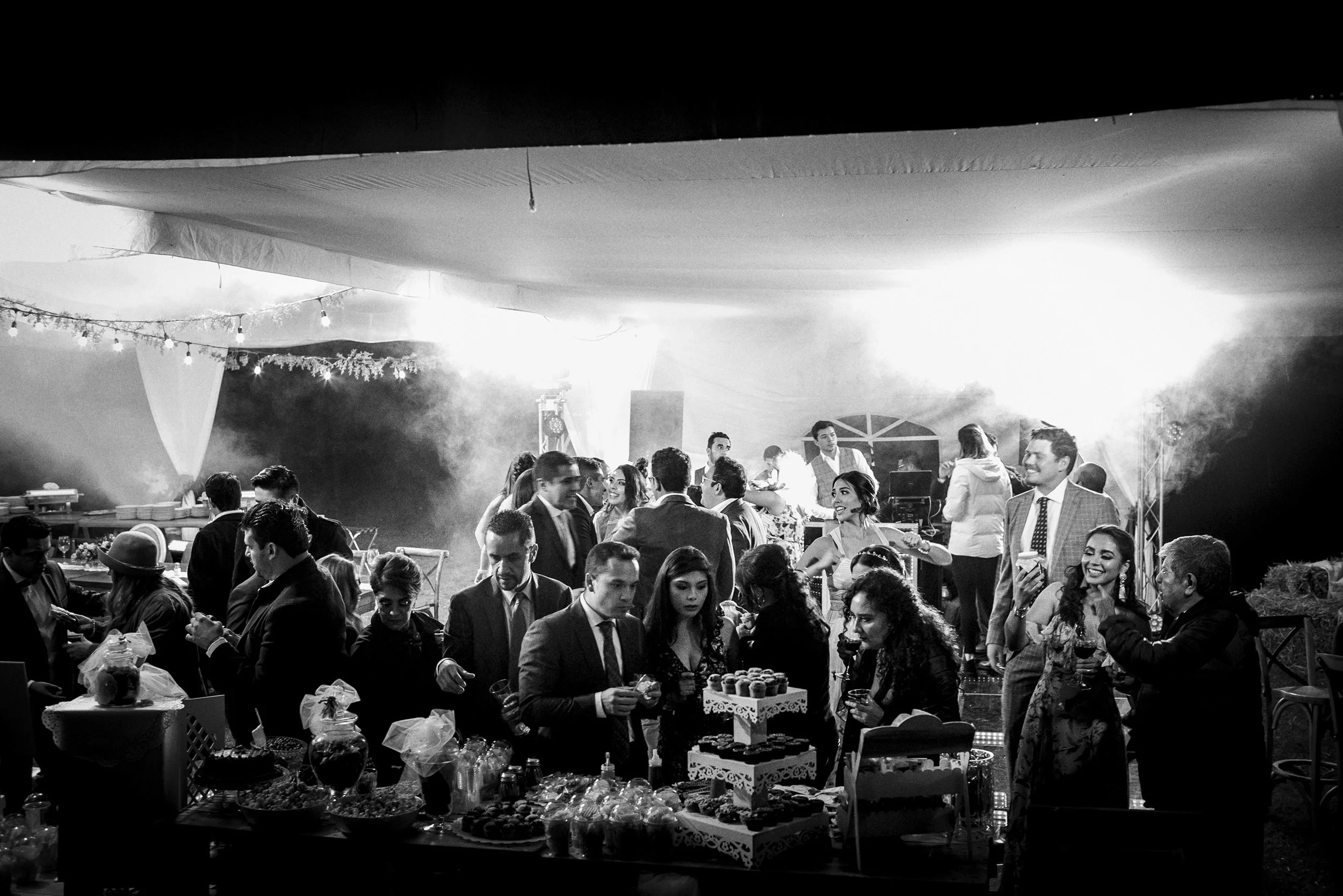 Fotografía documental en blanco y negro de invitados reunidos durante la recepción, ambiente social y espontáneo.