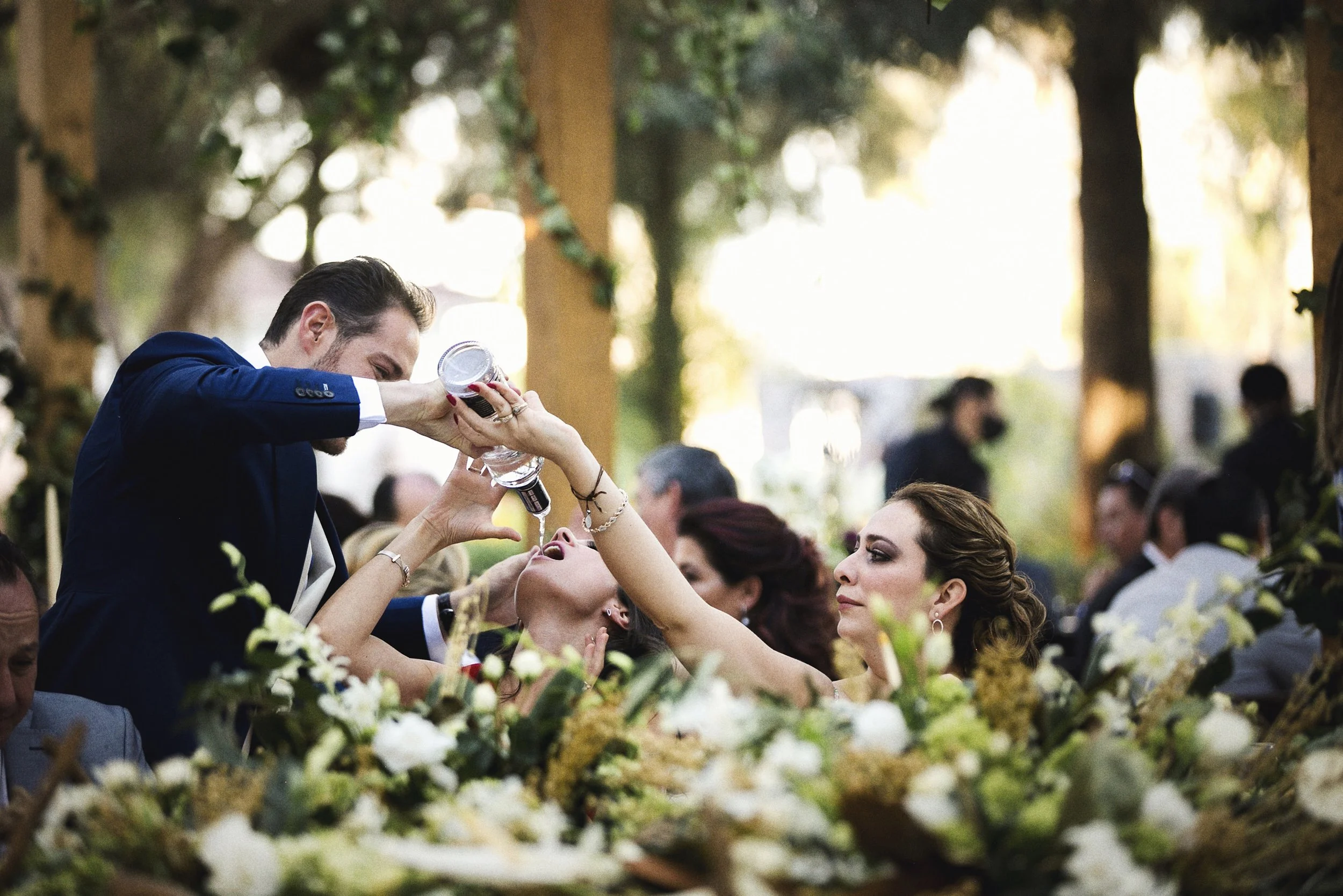 Fotografía documental de invitados celebrando durante la recepción, manos levantadas y flores en primer plano.