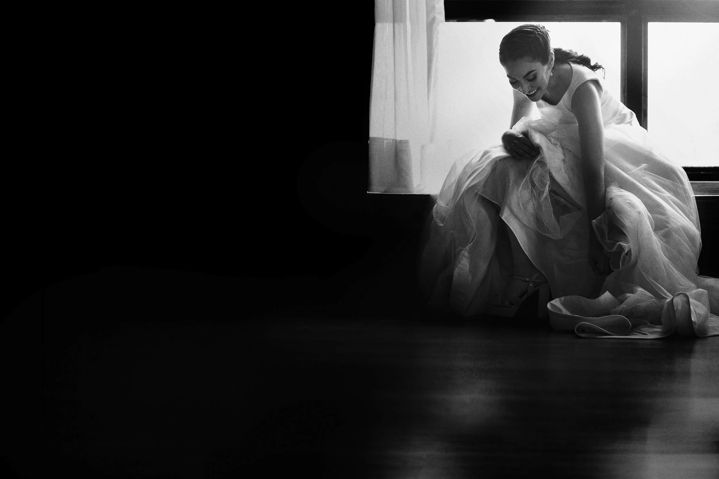 Fotografía en blanco y negro de novia sentada en interior, postura recogida y gesto íntimo.