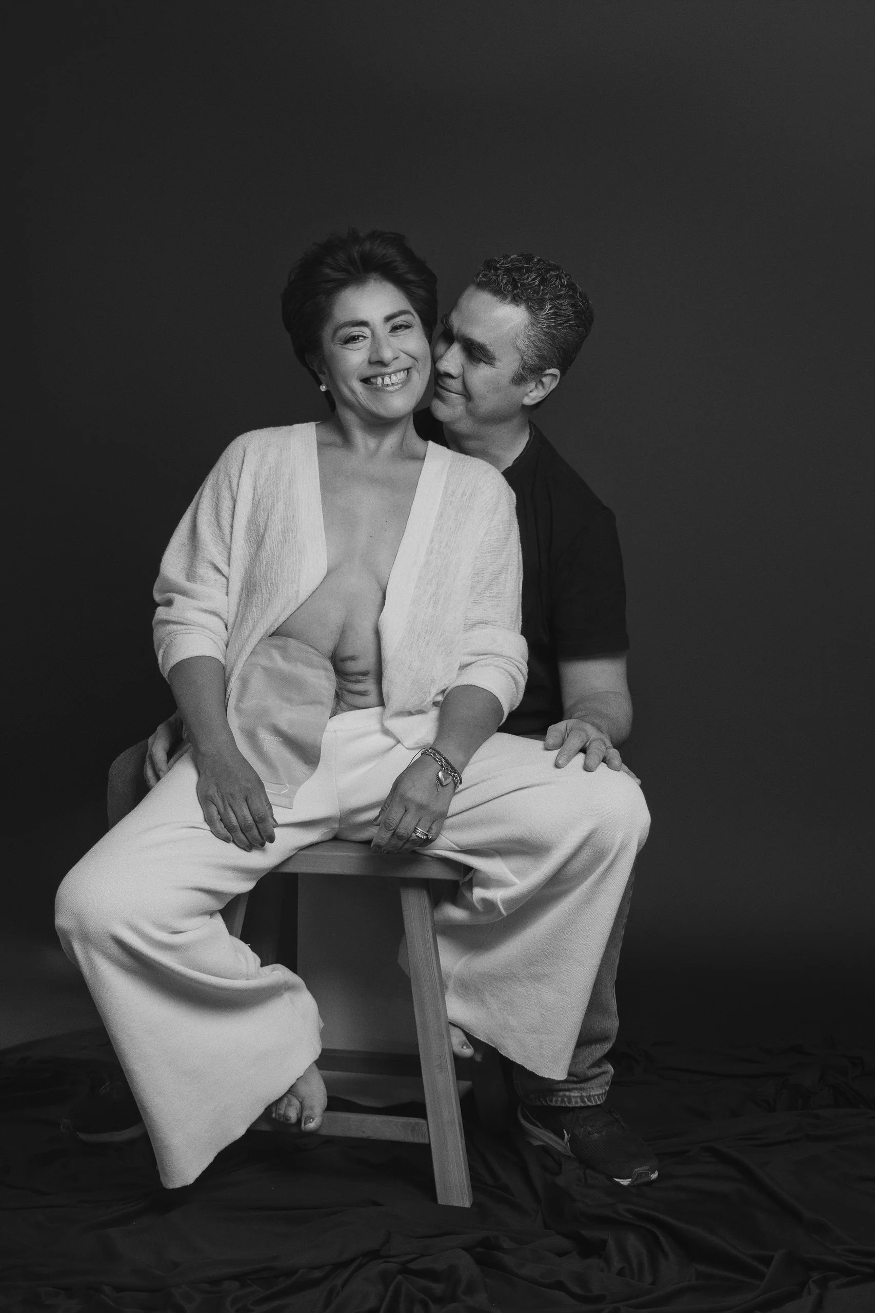 Retrato en blanco y negro de pareja sentada en estudio, gesto cercano y expresión natural.