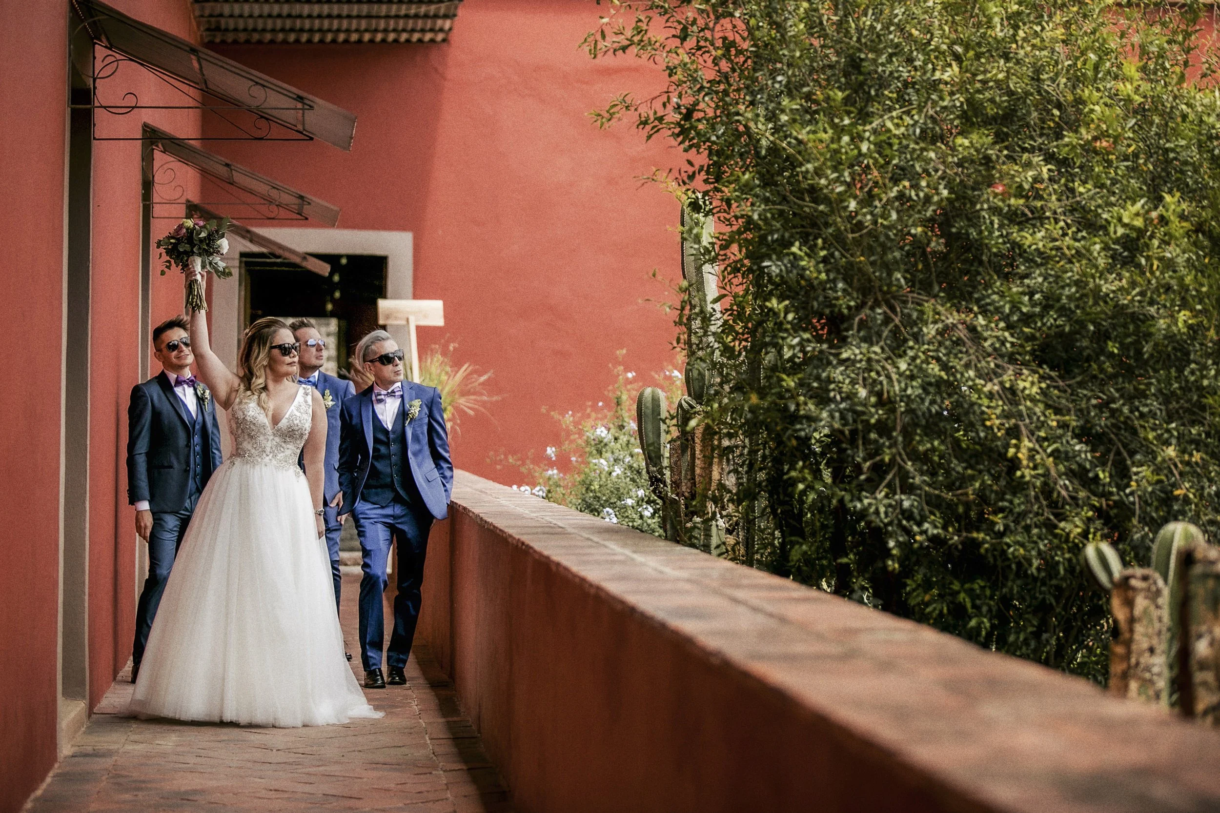 Fotografía de novios caminando juntos por pasillo exterior, acompañados por invitados.