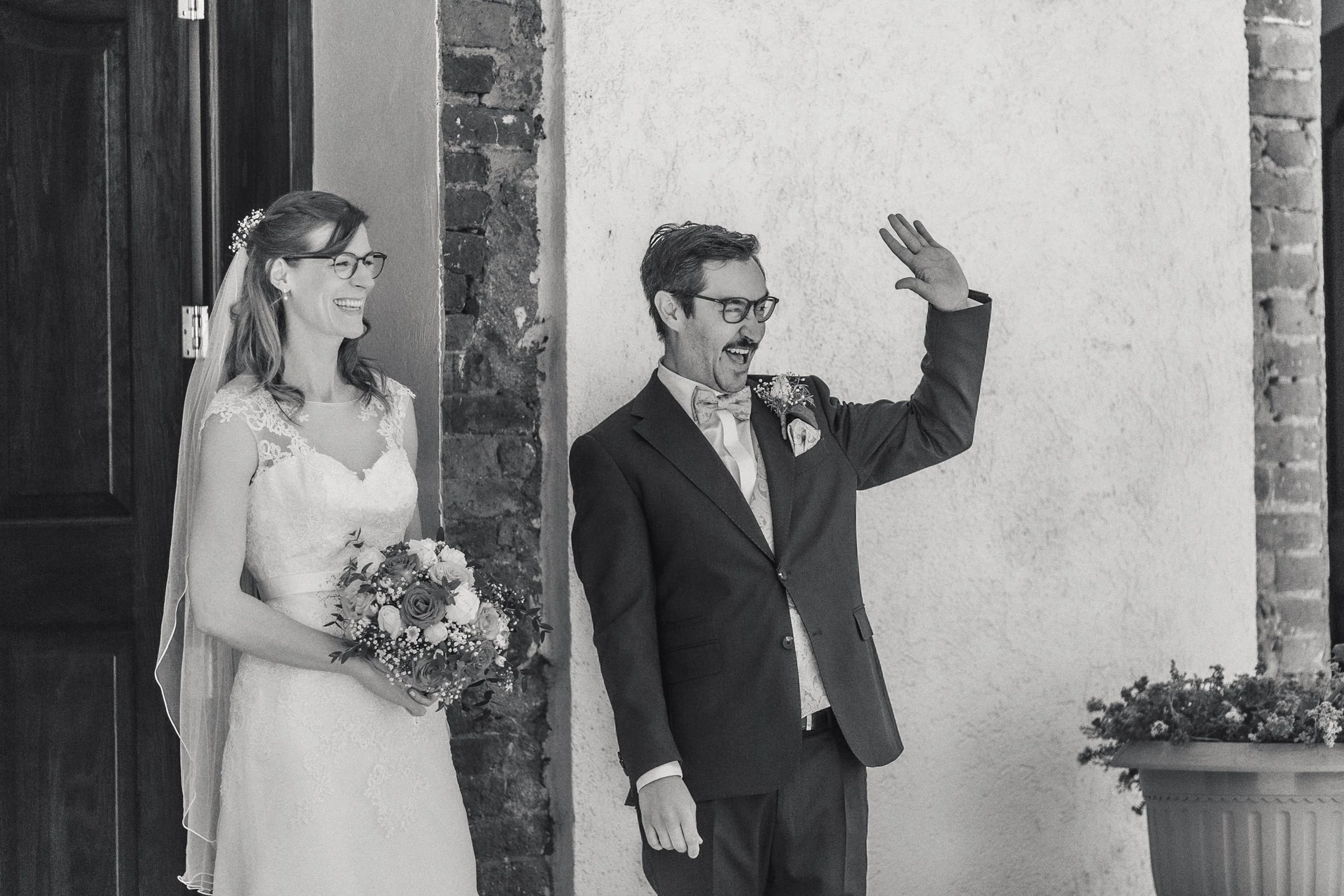 Fotografía en blanco y negro de novios saliendo del recinto, saludo a invitados.