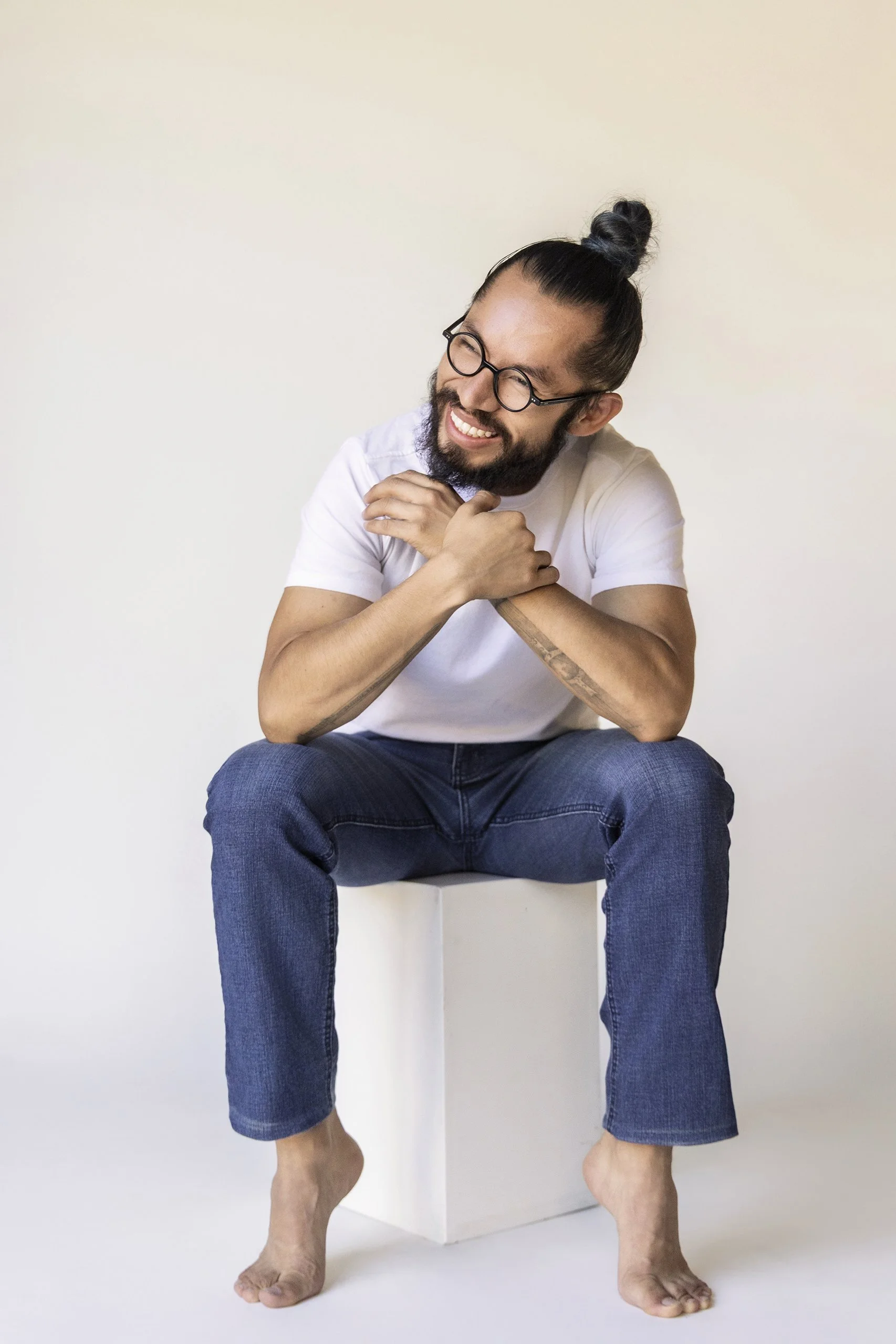 Retrato de hombre sentado en estudio, vestimenta casual, brazos cruzados y sonrisa abierta.