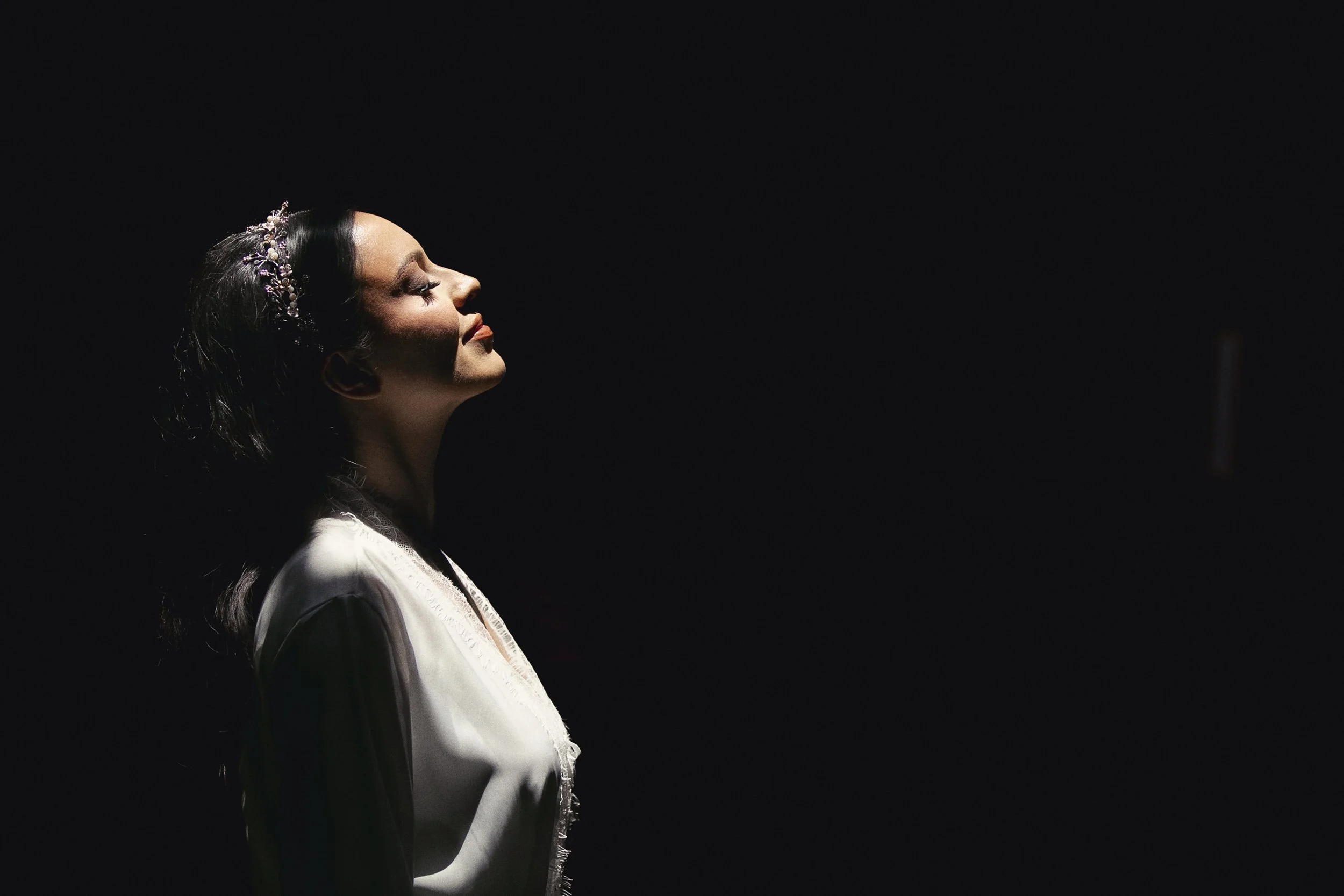 Fotografía en blanco y negro de novia mirando hacia arriba, luz lateral y expresión contenida.