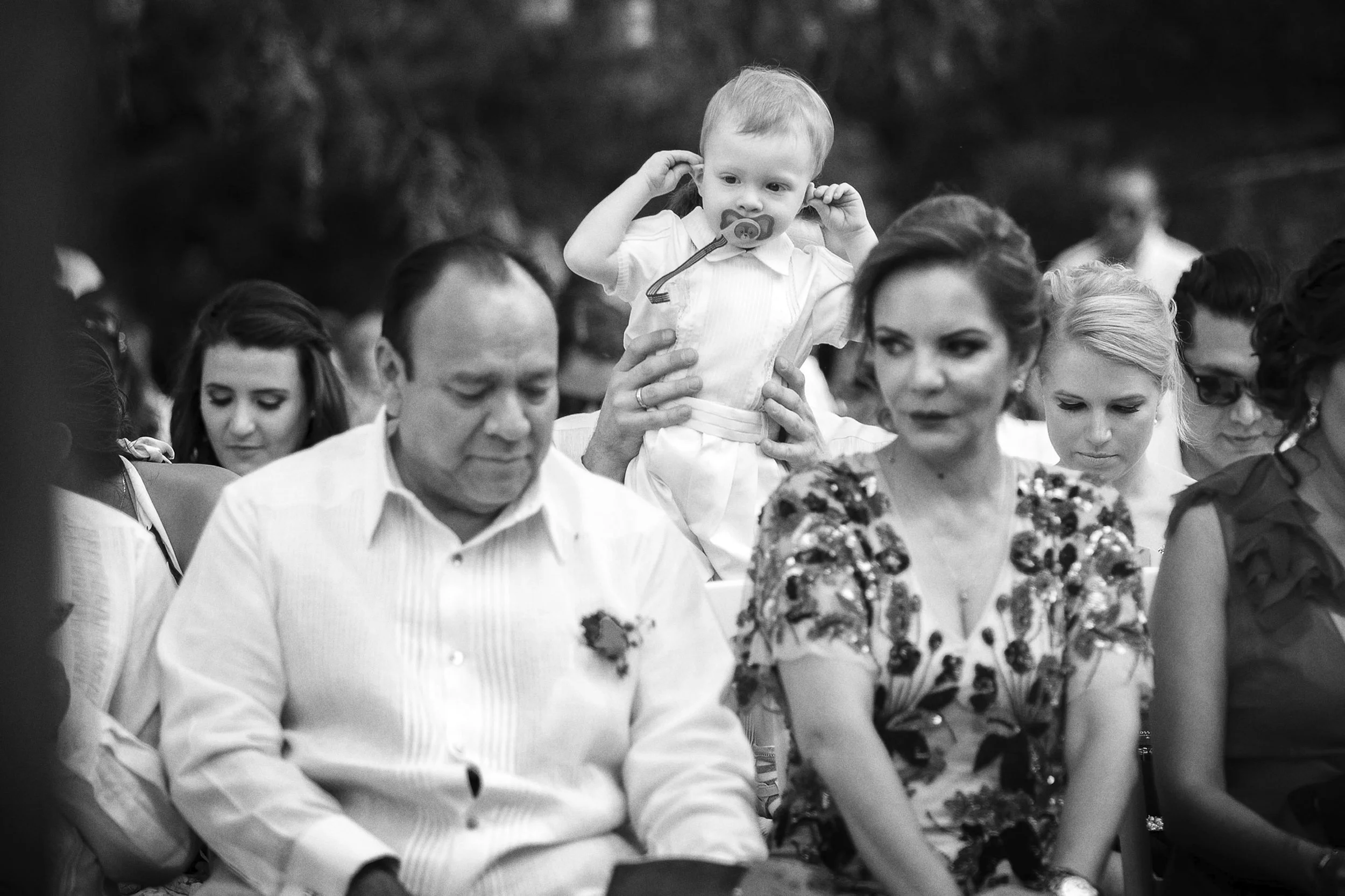 Fotografía documental en blanco y negro de familia cargando a bebé durante la celebración.