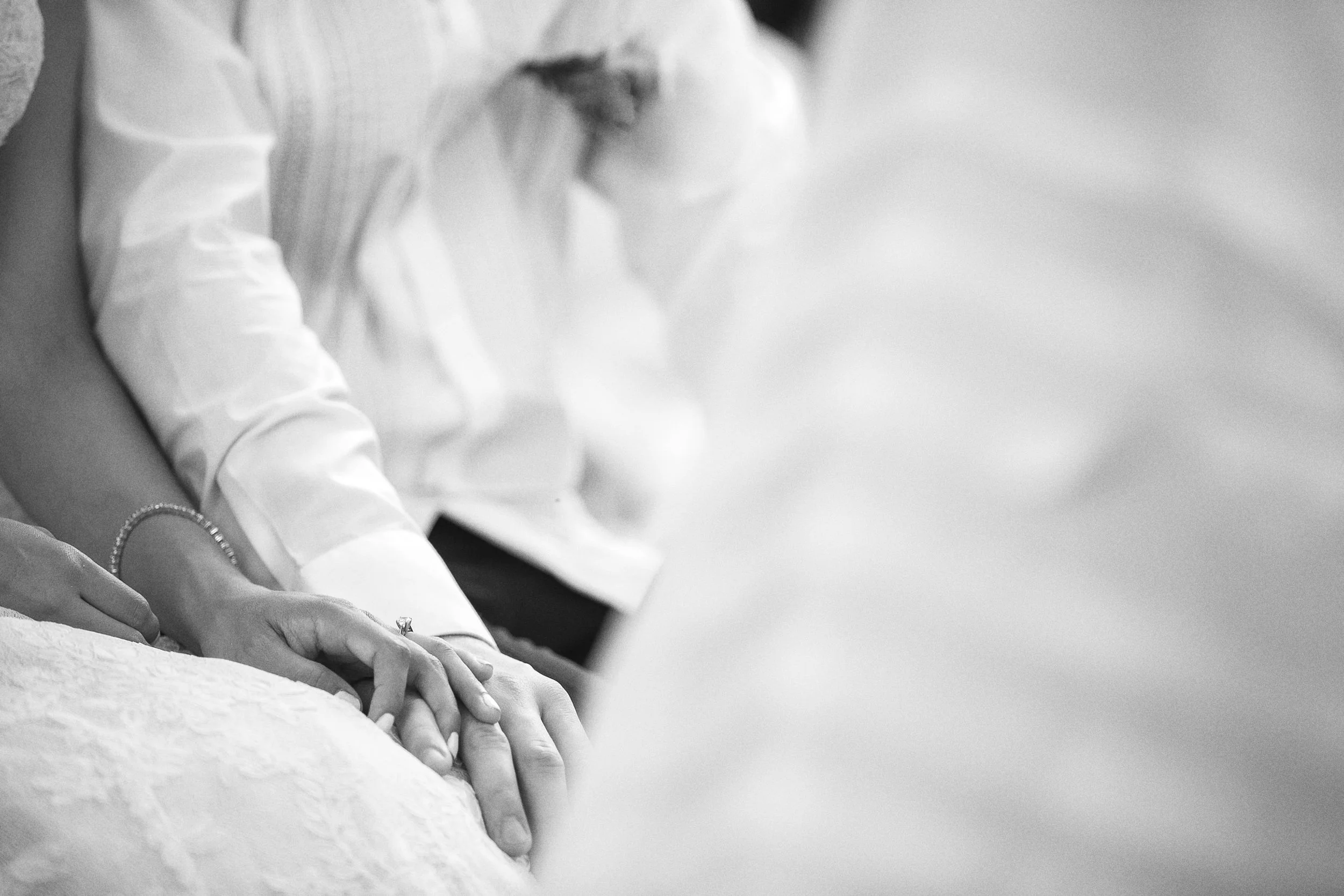 Fotografía en blanco y negro de manos entrelazadas durante la ceremonia, detalle íntimo.