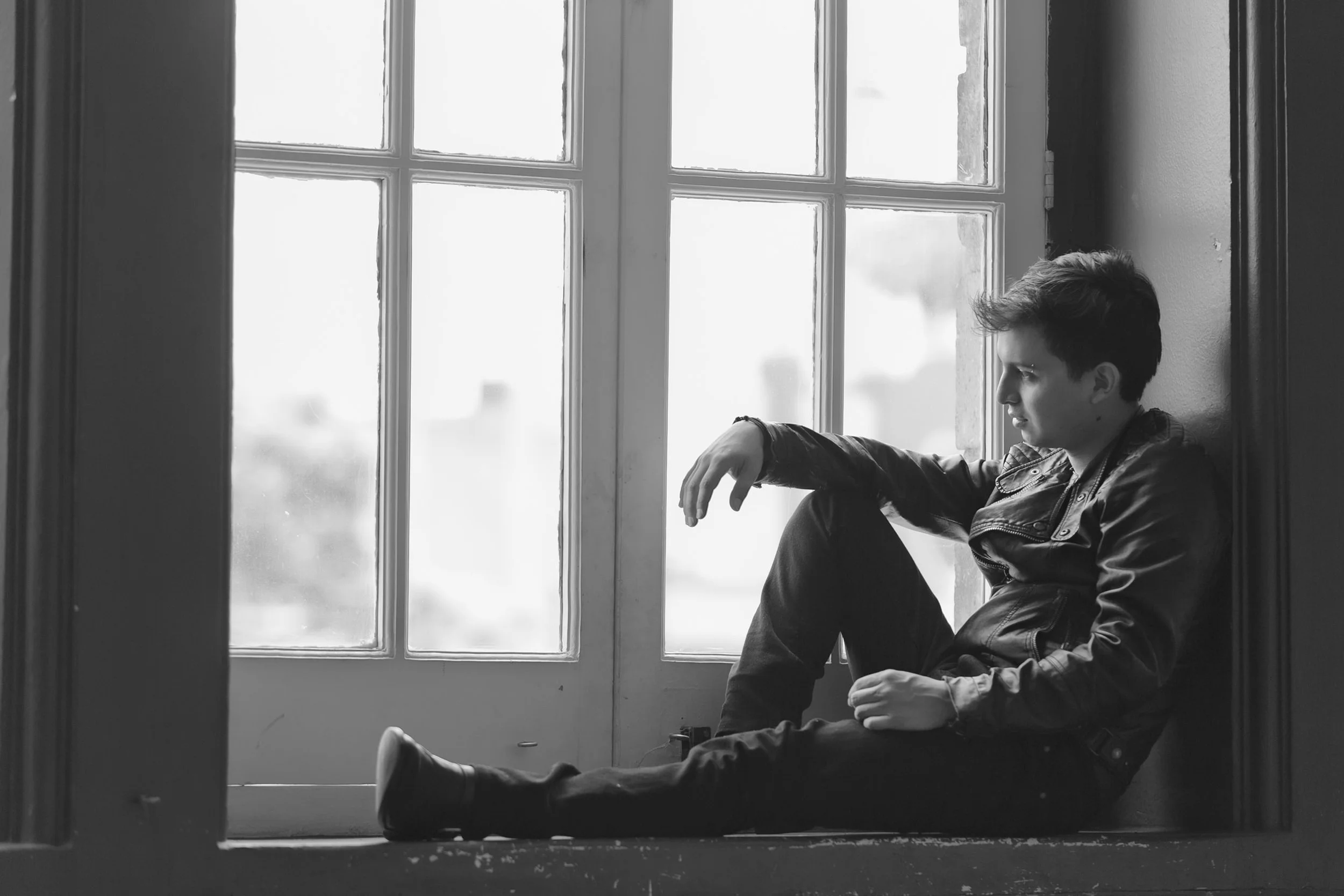 Retrato en blanco y negro de hombre sentado junto a ventana, gesto introspectivo y luz natural.