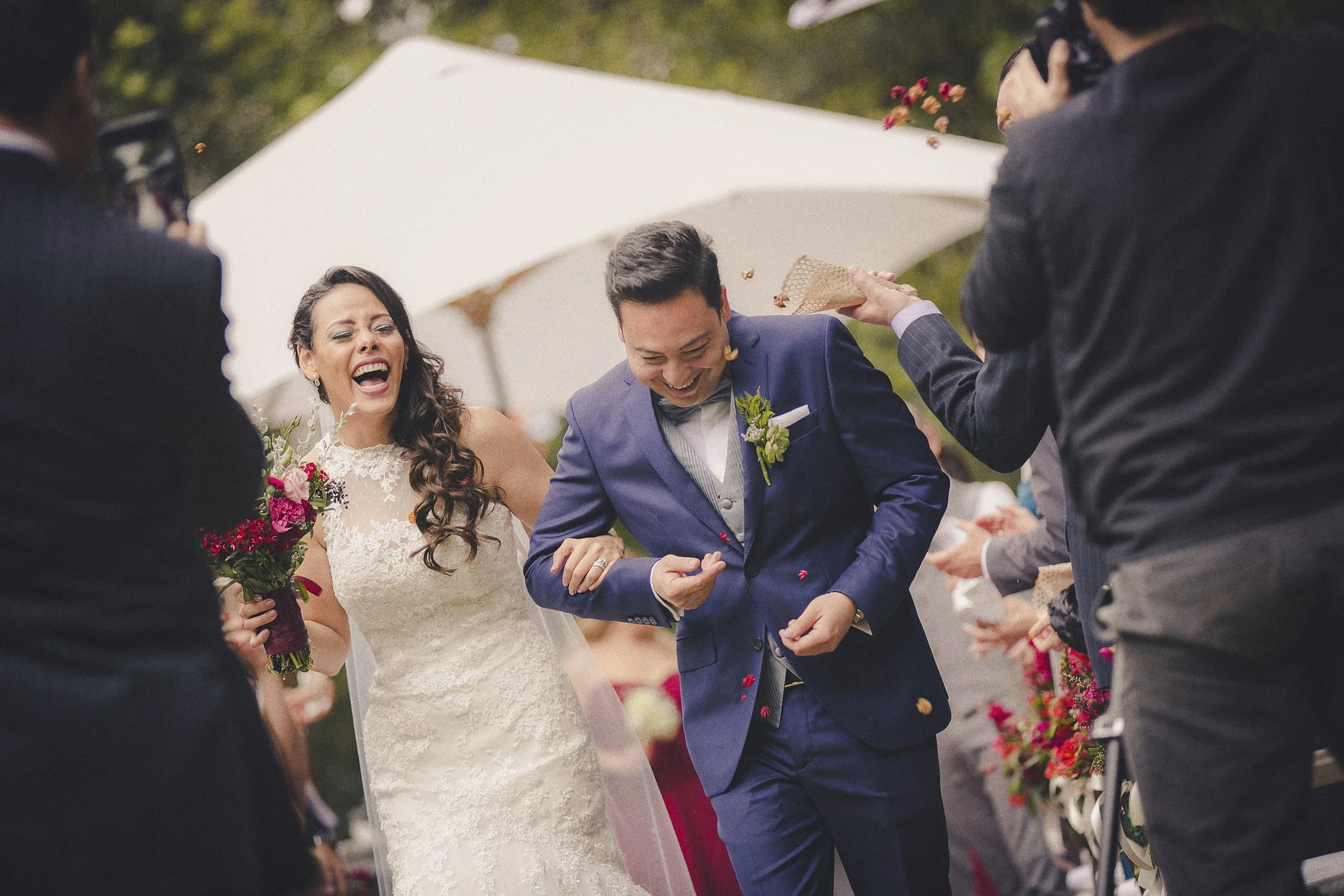Fotografía documental de novios caminando entre invitados mientras reciben pétalos.