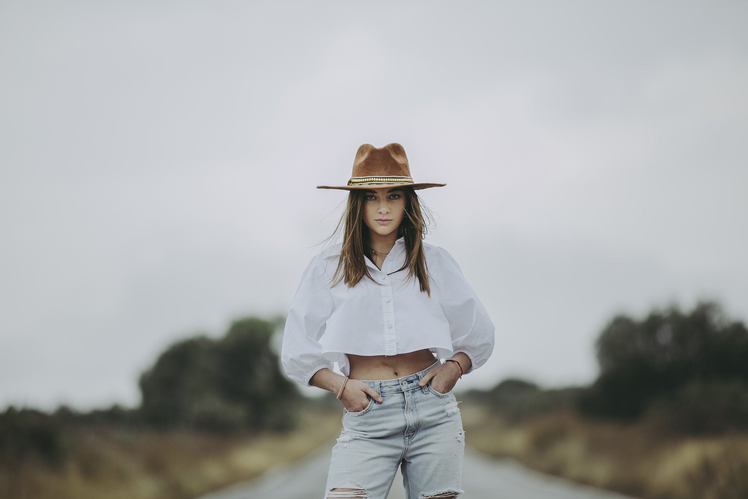 Retrato de mujer en exterior con sombrero, fondo natural desenfocado y expresión serena.