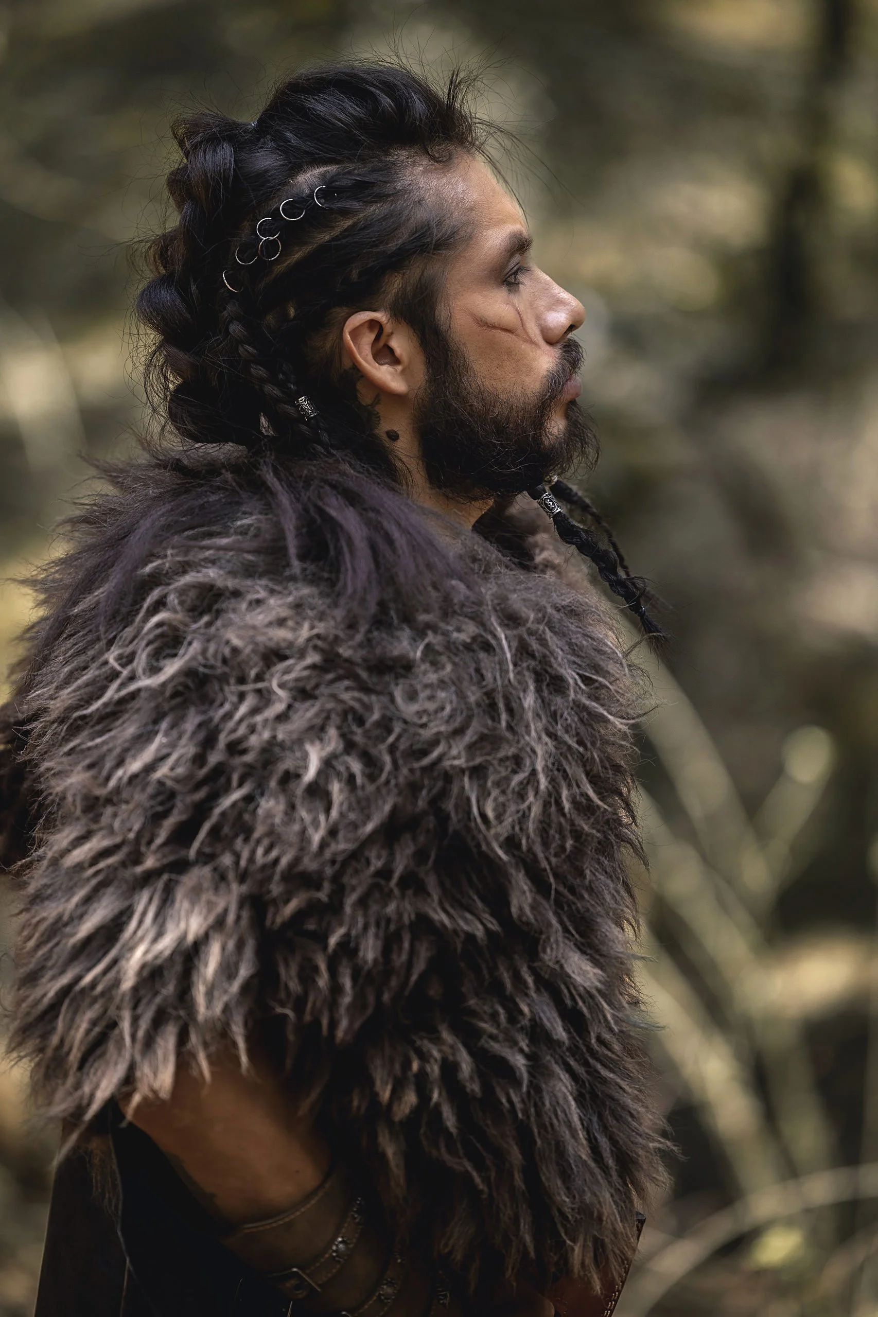 Retrato de hombre de perfil en exterior, vestimenta con textura de piel y mirada hacia el entorno natural.