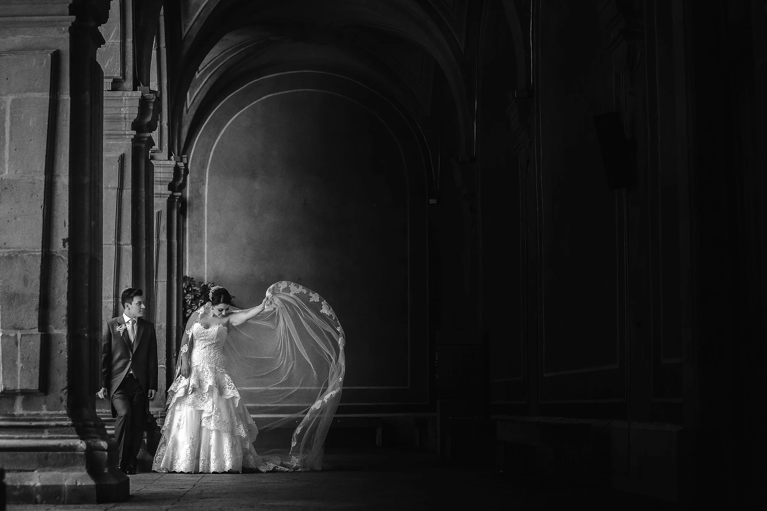 Fotografía en blanco y negro de novia sola en espacio arquitectónico, vestido extendido y atmósfera contemplativa.