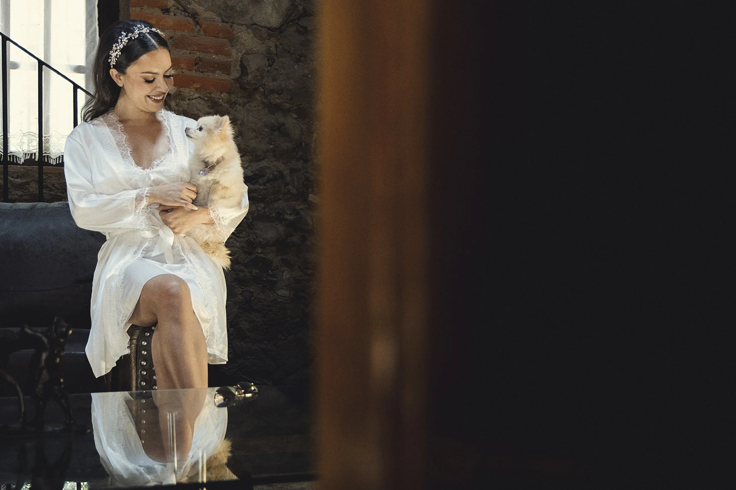 Fotografía de novia sentada en interior, vestida de blanco, mirada hacia abajo y gesto tranquilo.