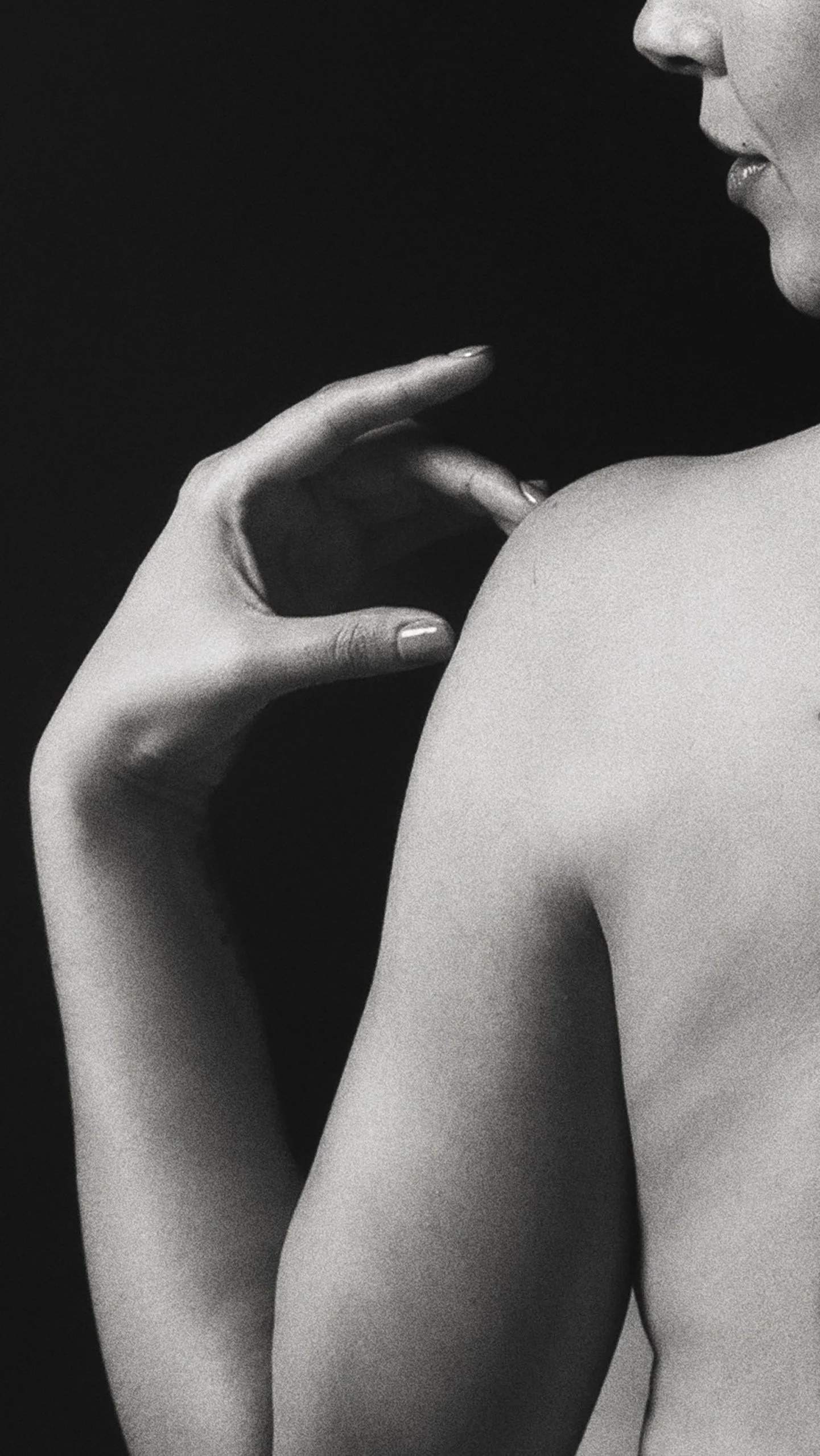 Detalle en blanco y negro de mano tocando suavemente un hombro, gesto íntimo.