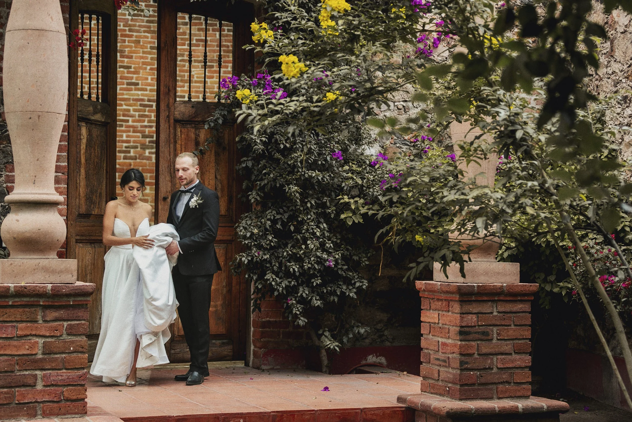 Fotografía documental de novios de pie frente a arquitectura del lugar, pausa previa al siguiente momento.