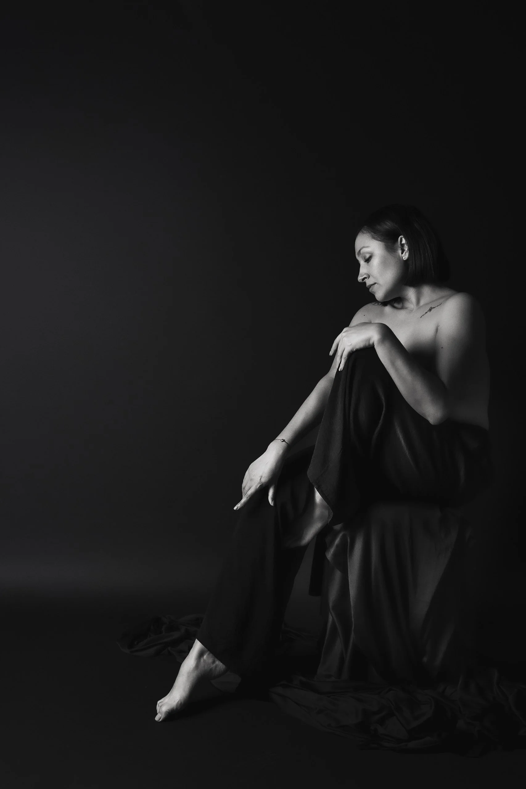 Retrato en blanco y negro de mujer sentada en el suelo, postura recogida y gesto introspectivo.