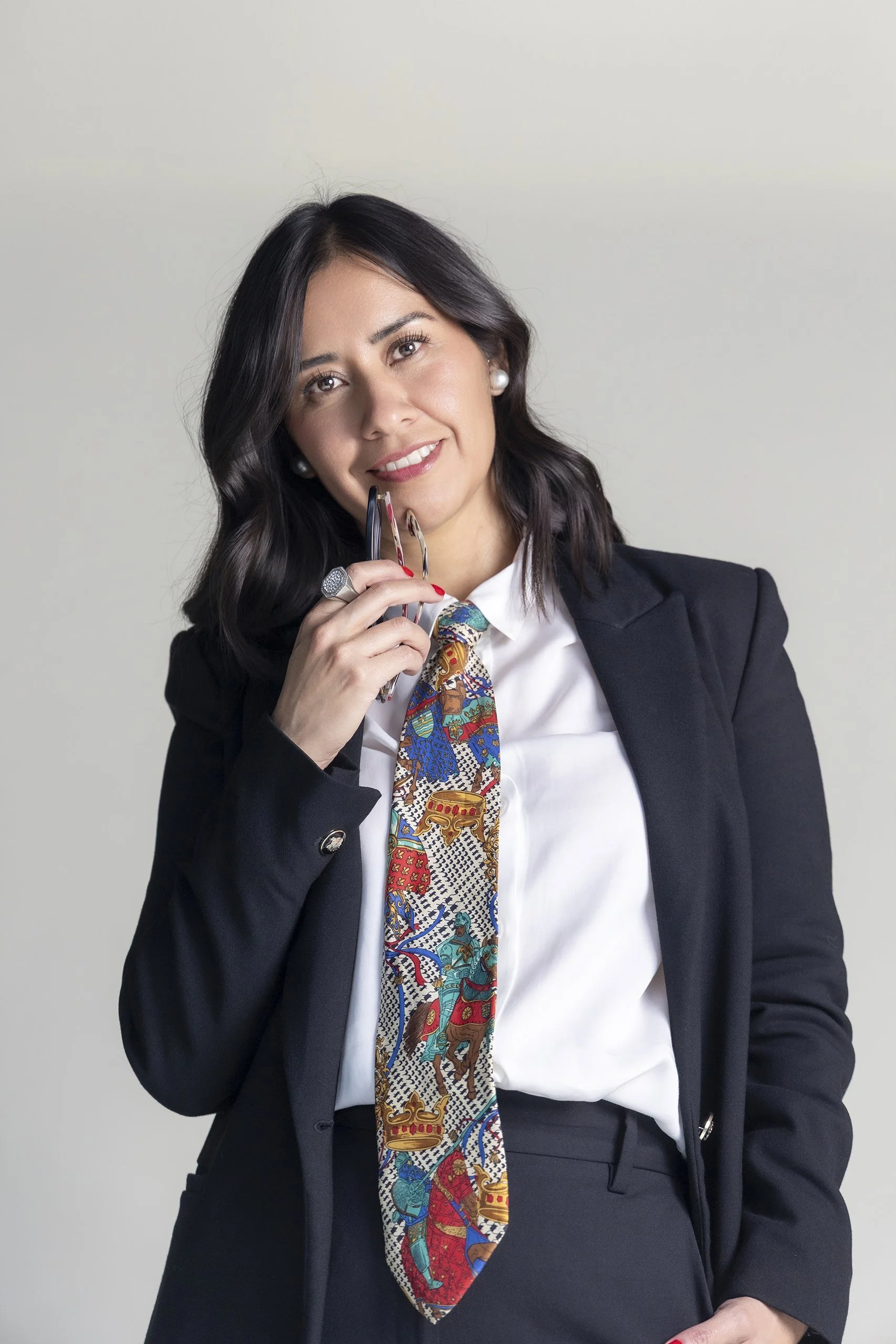 Retrato de mujer con traje formal y corbata de colores, expresión segura y gesto espontáneo en estudio.