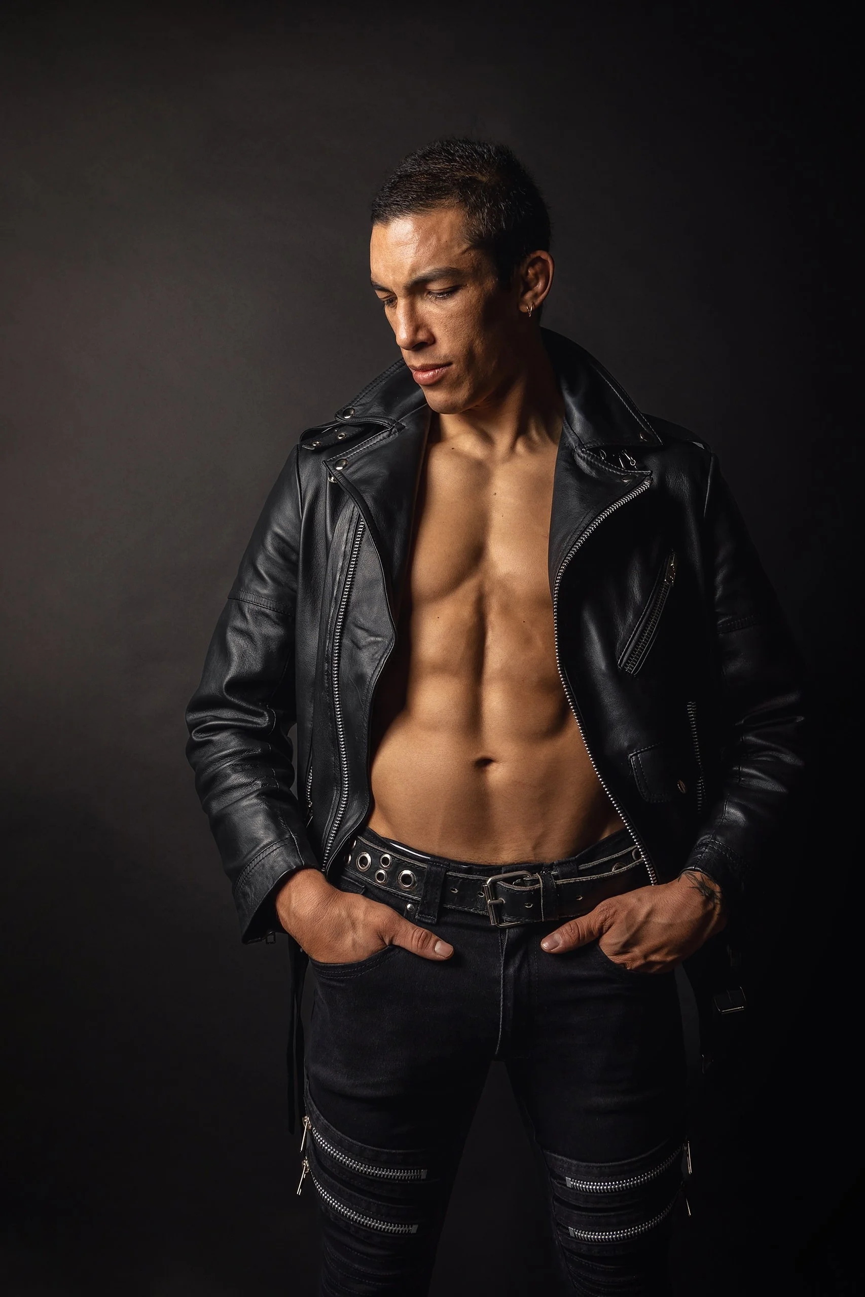 Retrato de hombre en estudio con chaqueta de piel, torso descubierto y postura firme.