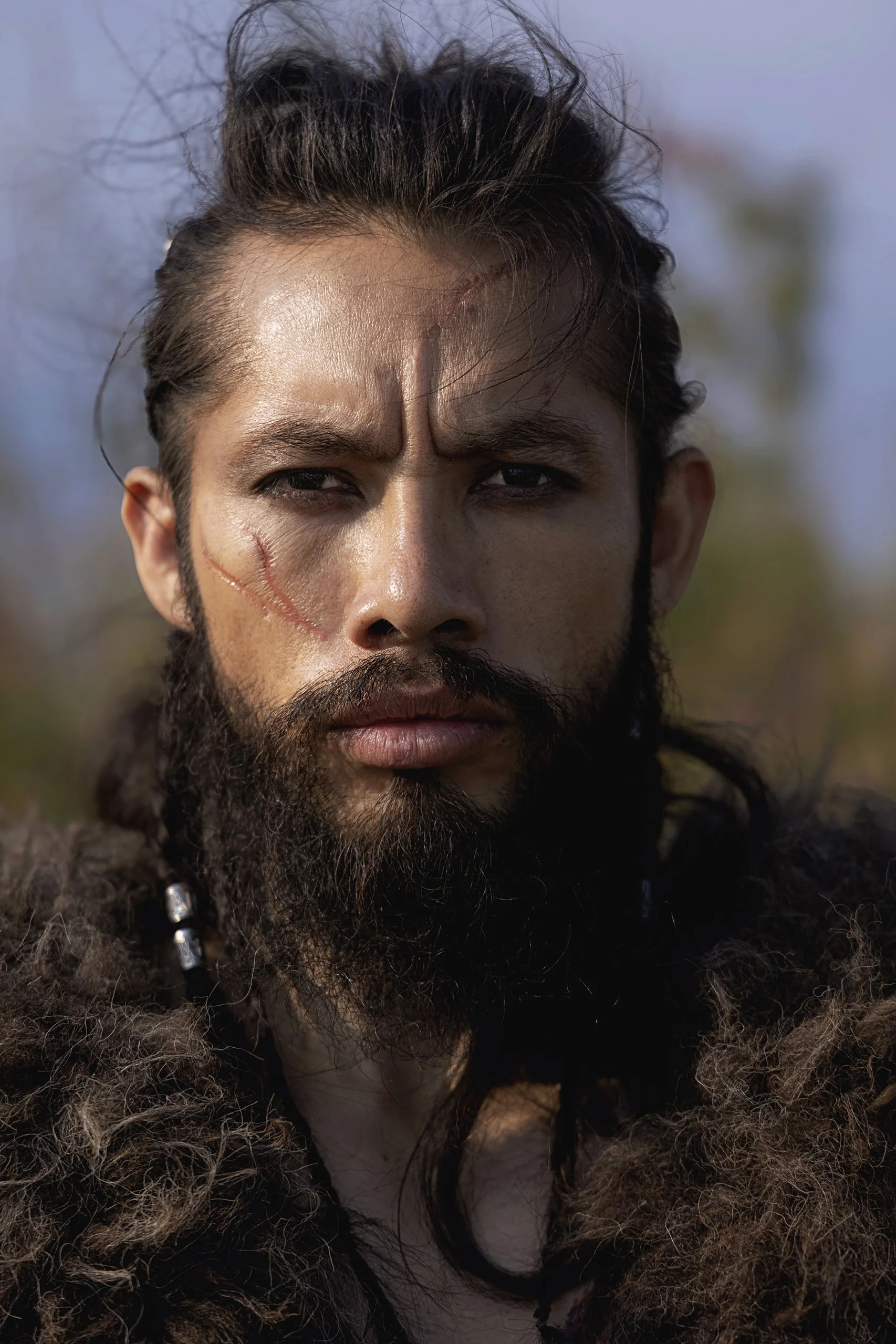 Primer plano de hombre en exterior, rostro con marcas visibles y mirada directa.