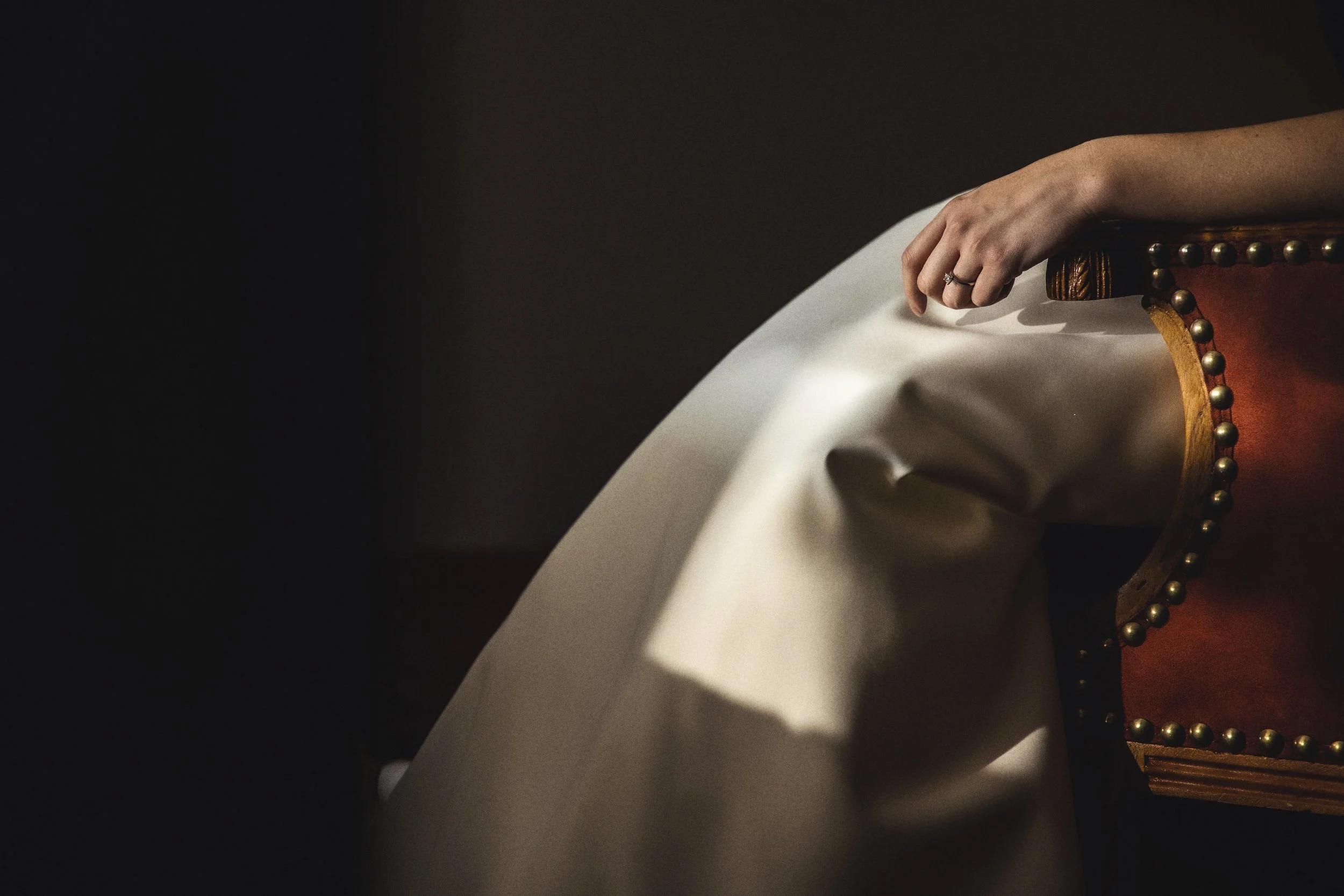 Detalle de mano sobre tela del vestido de novia, luz suave y textura visible.
