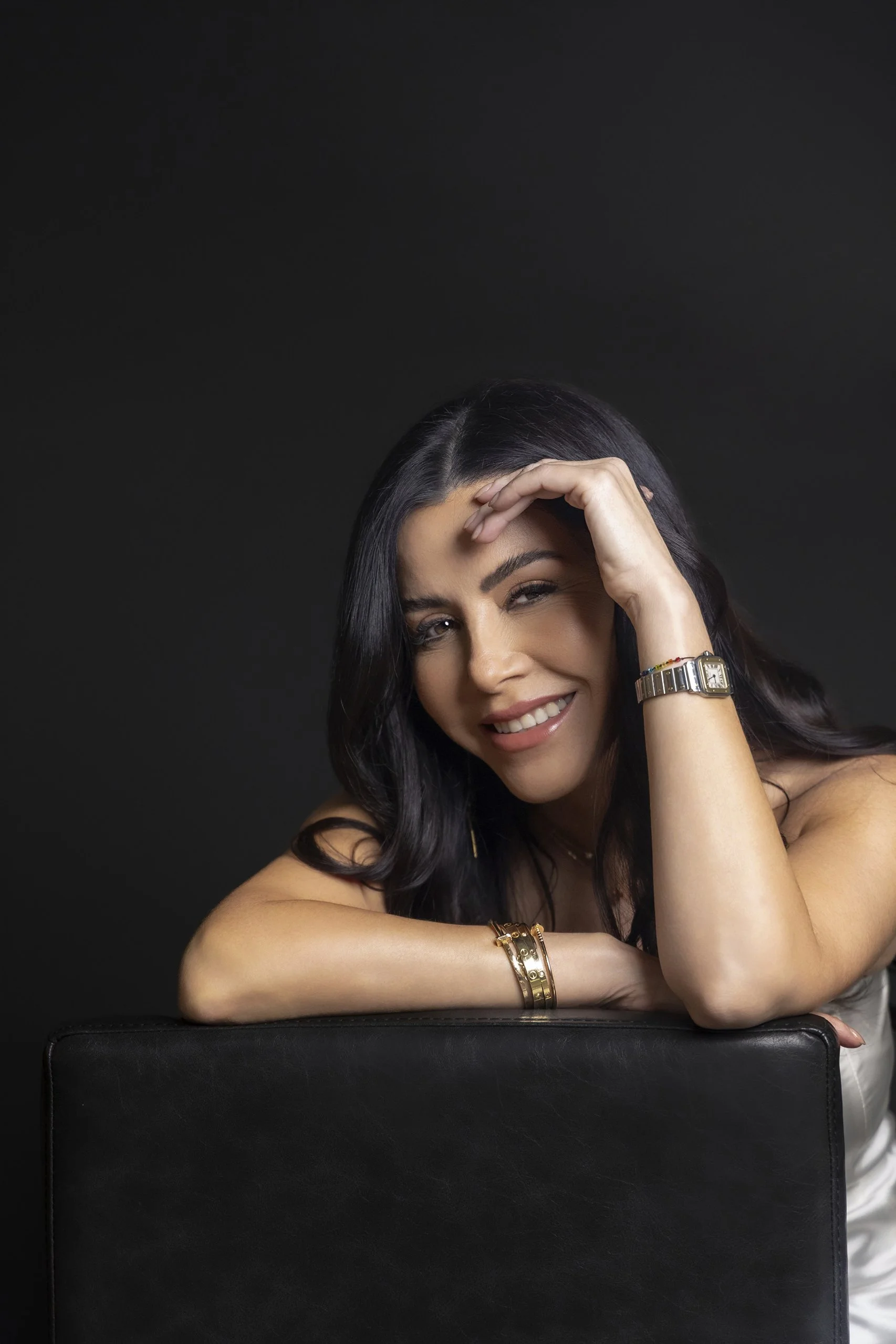 Retrato de mujer apoyada sobre superficie, sonrisa suave y gesto relajado en estudio.