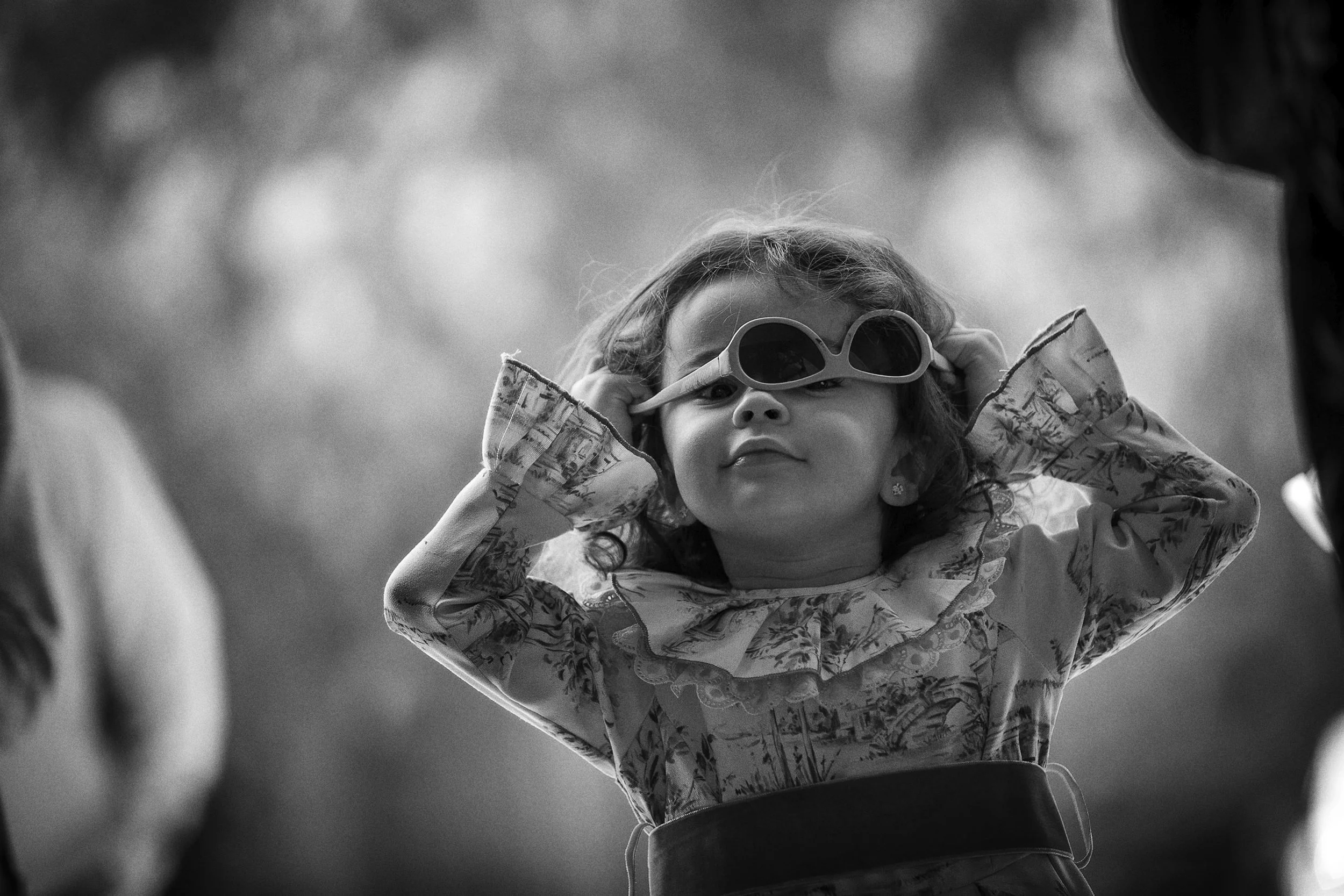 Fotografía en blanco y negro de niña con lentes de sol, gesto espontáneo durante la celebración.