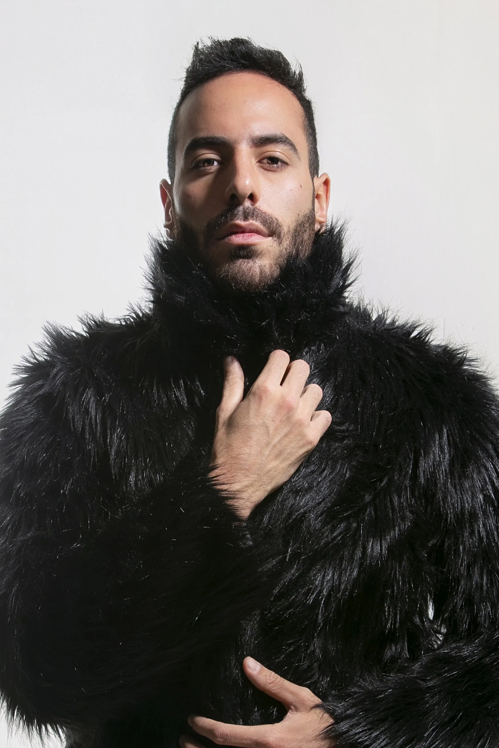 Retrato de hombre en estudio con vestimenta oscura de textura, mirada directa y postura frontal.
