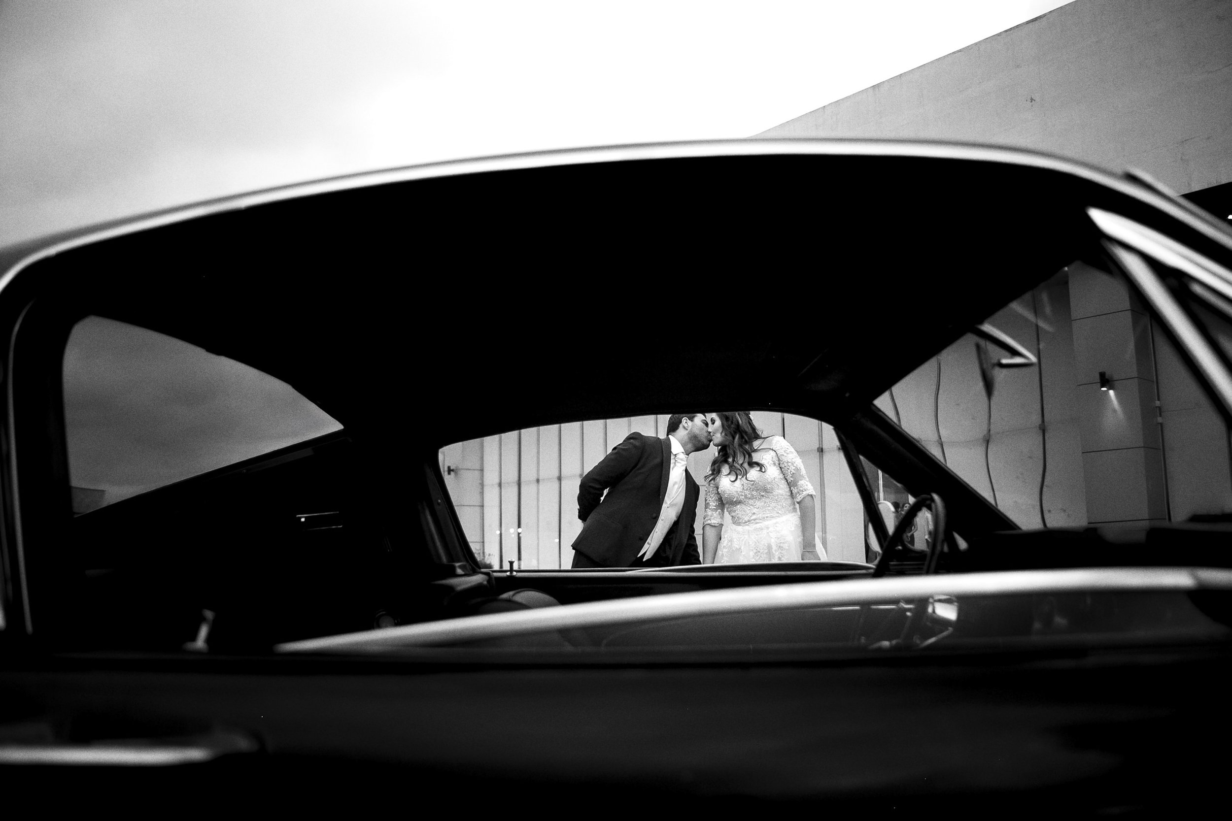 Fotografía documental en blanco y negro de novios vistos a través de la ventana de un automóvil.