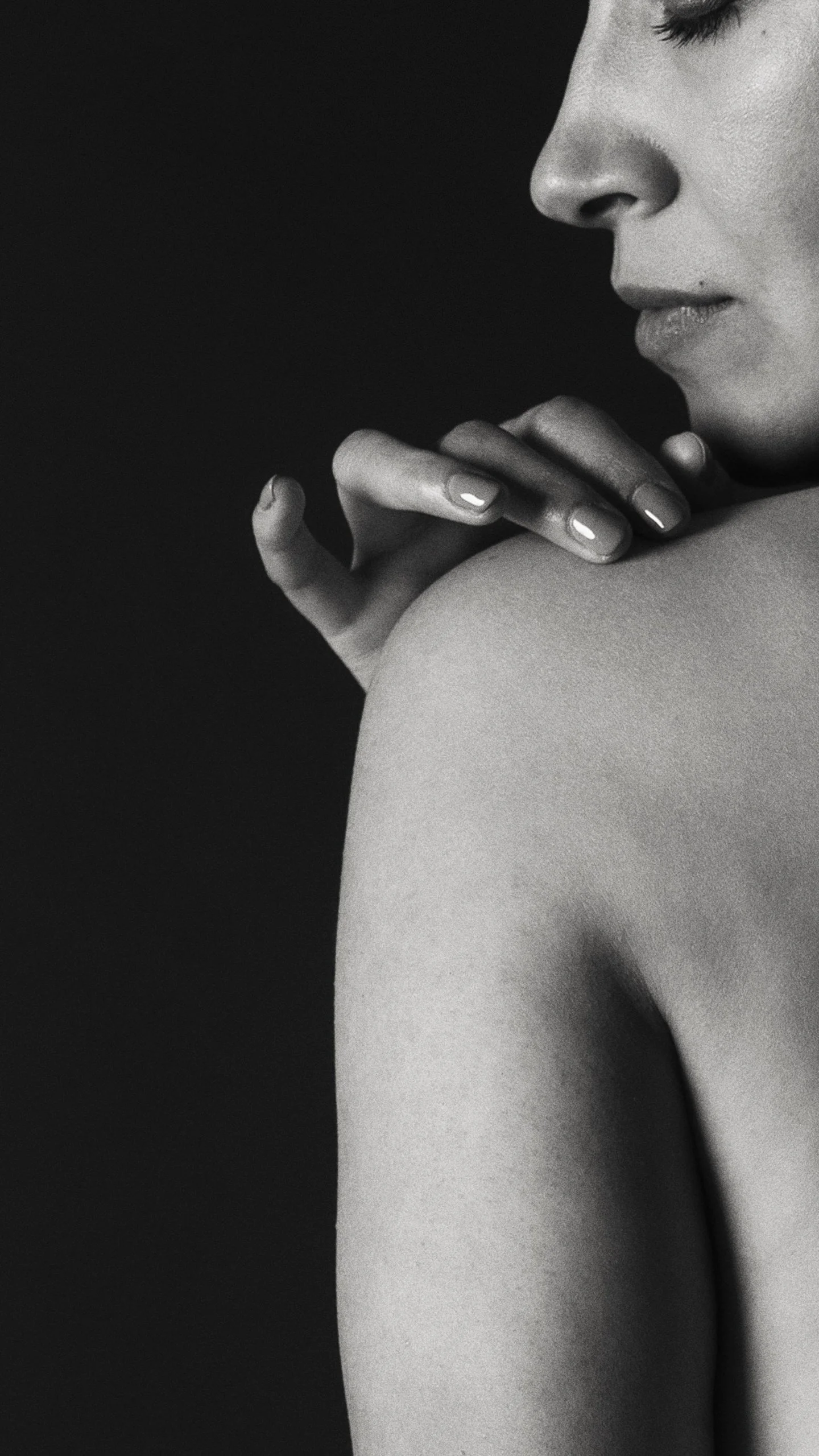 Detalle en blanco y negro de mano apoyada sobre espalda, textura de piel y gesto íntimo.