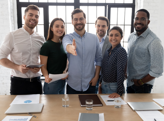Group of six diverse professionals smiling and having a meeting in a modern office, with documents and tablets on the table.