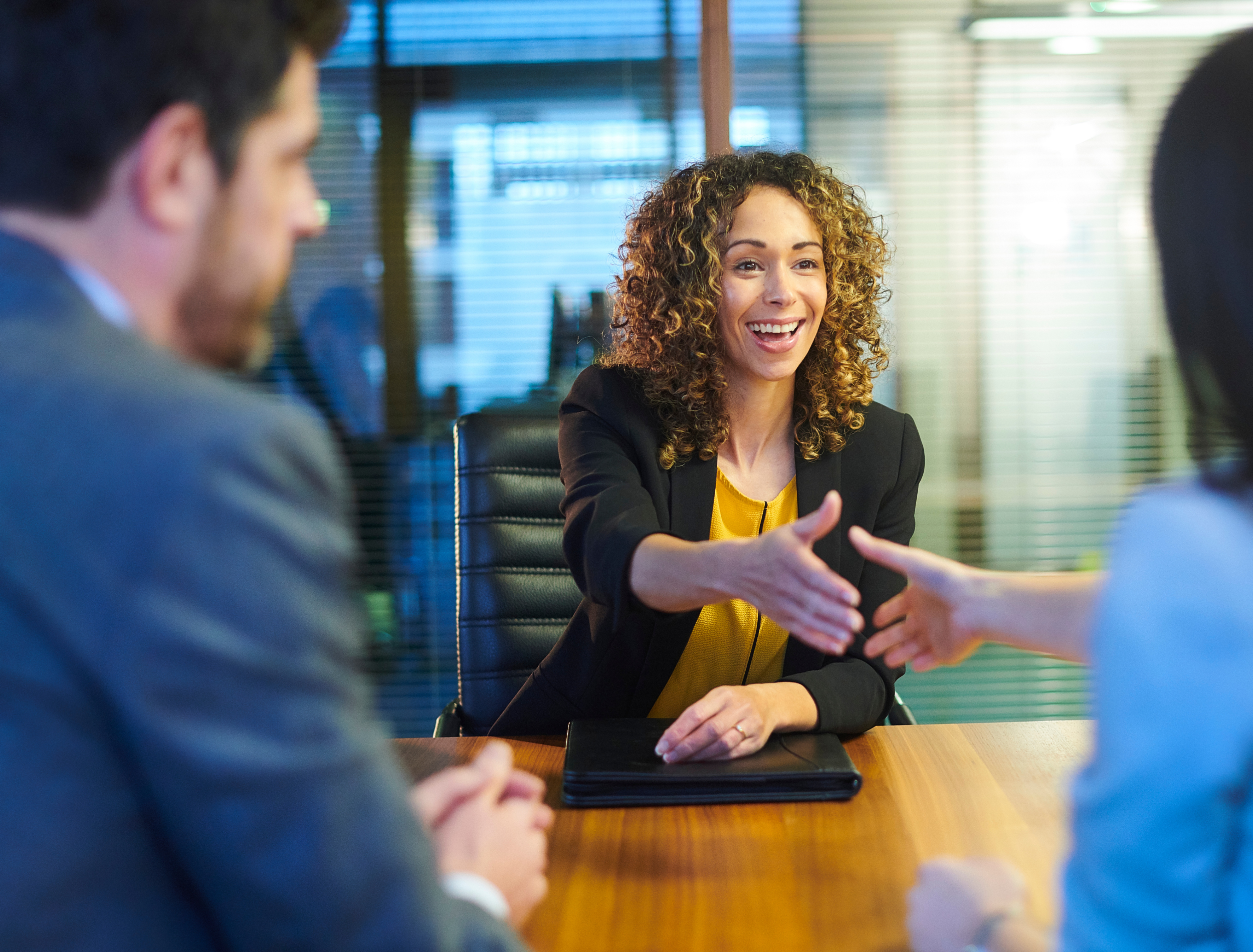 Businesswoman smiling and shaking hands with a colleague during a meeting in a conference room.