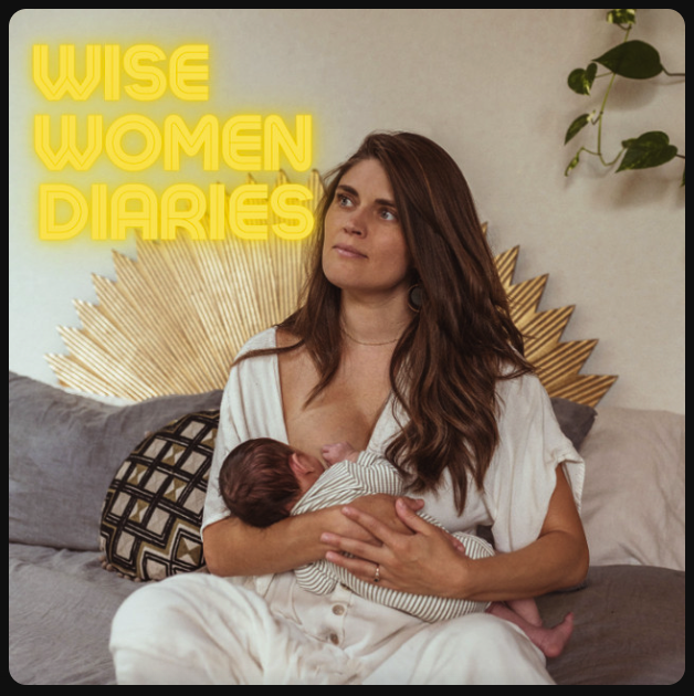 A woman breastfeeding a baby on a gray couch, with decorative pillows and a golden sunburst wall art in the background.