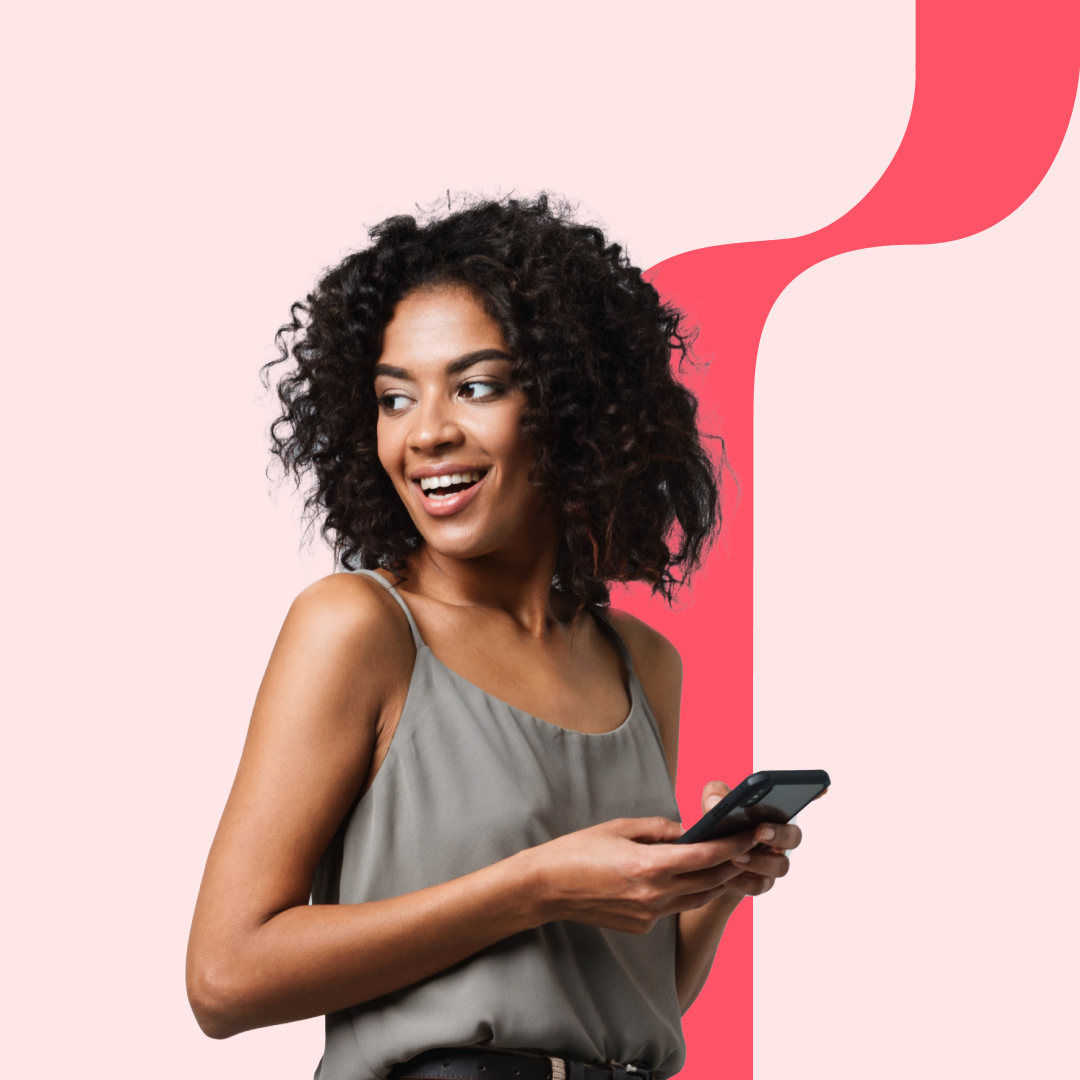 A young woman with curly hair smiling and holding a smartphone, standing against a pink background with a red abstract shape.