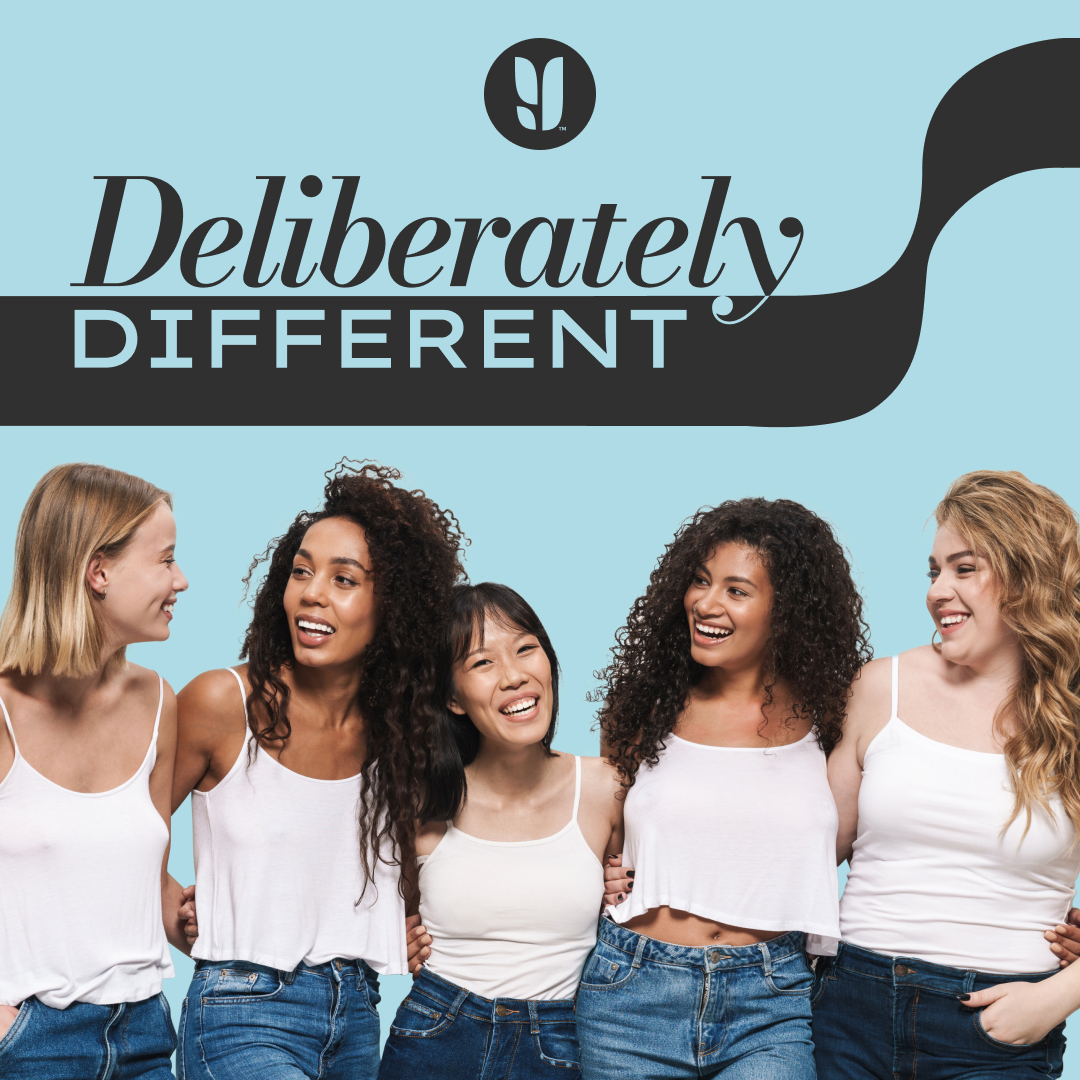 A diverse group of five women smiling and standing together against a light blue background with the words 'Deliberately Different' visible at the top.