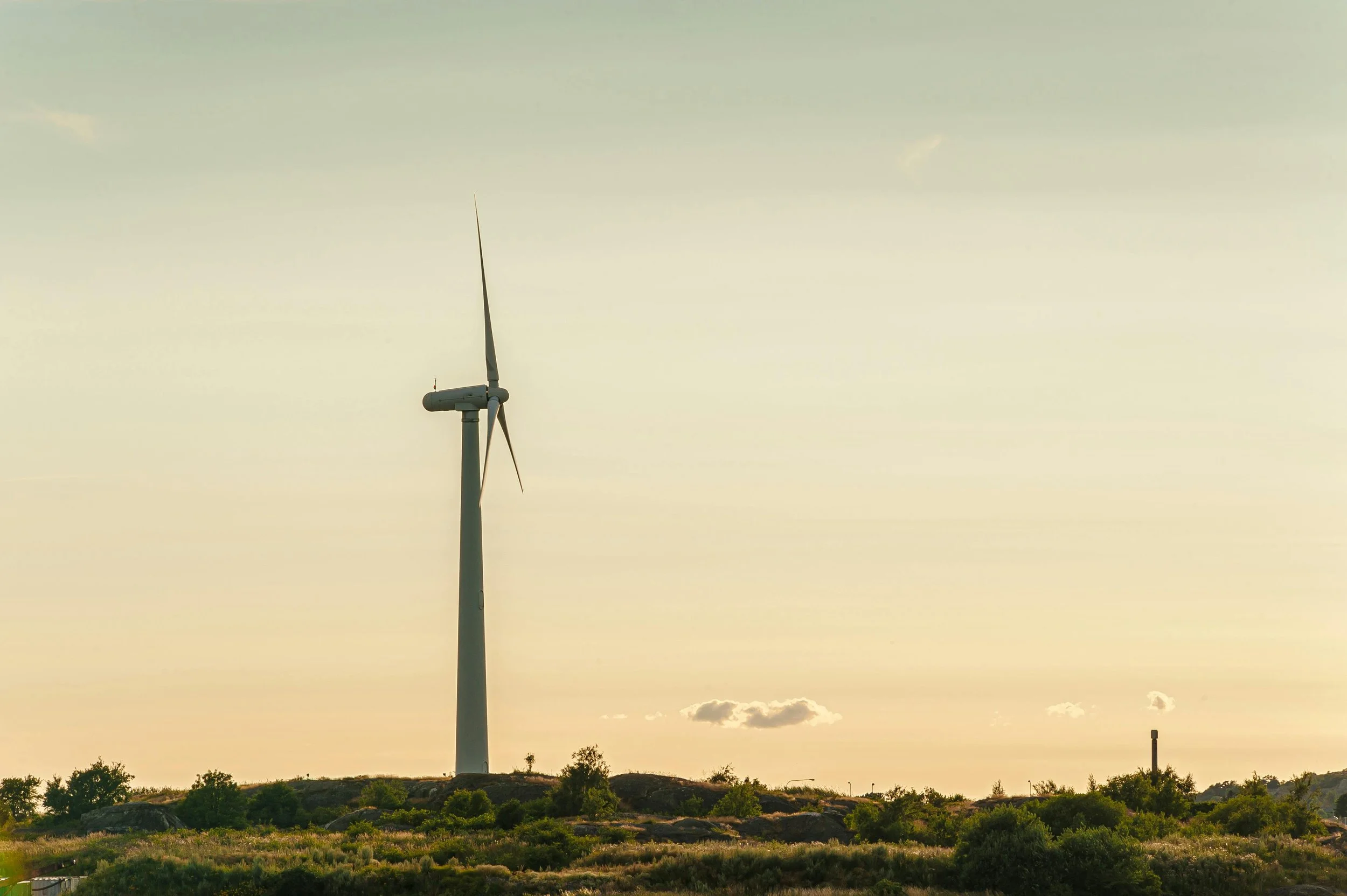 A wind turbine on a hilltop during sunset with a few clouds in the sky.