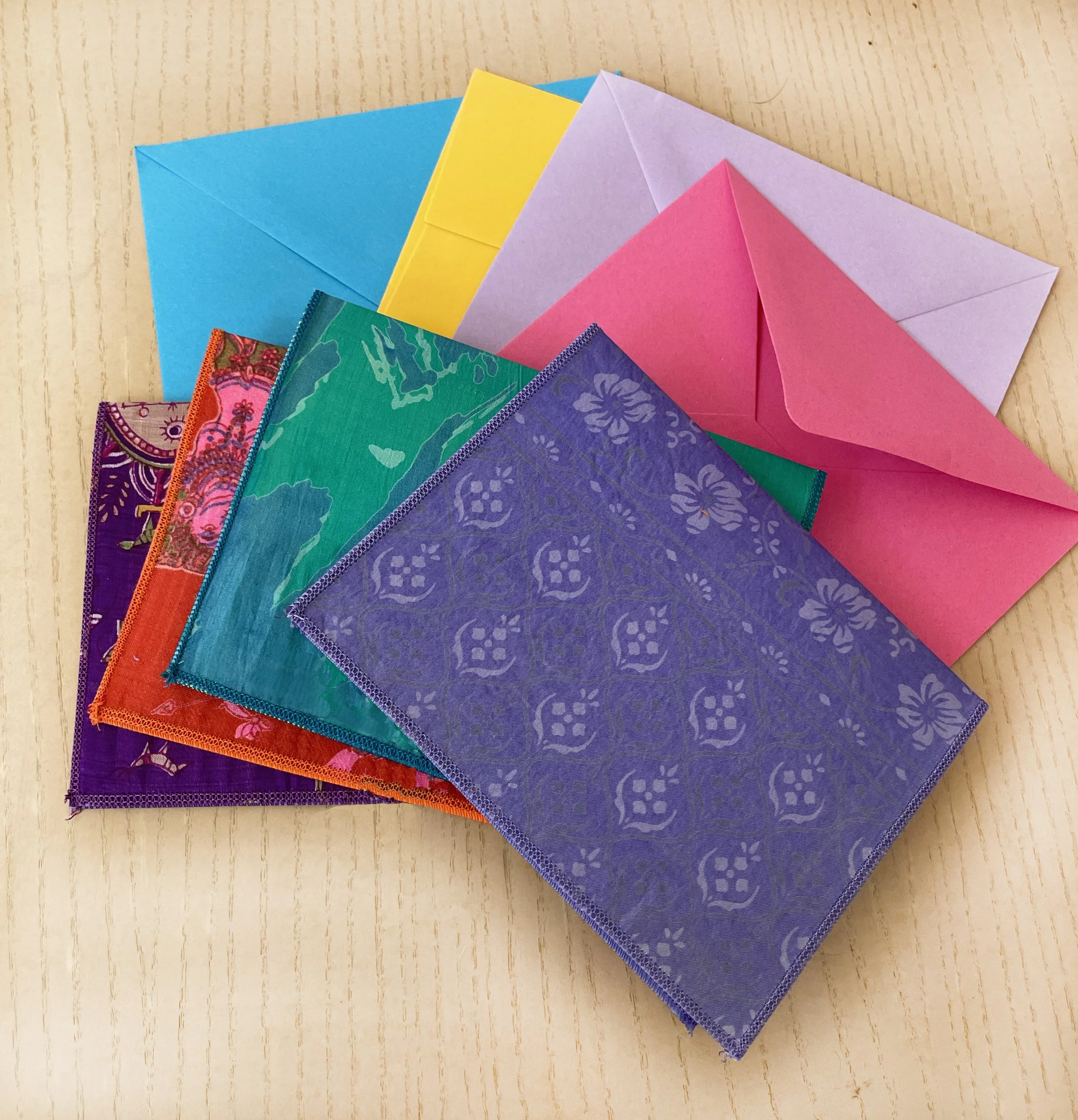 Colored fabric squares and pastel paper envelopes arranged on a wooden surface.