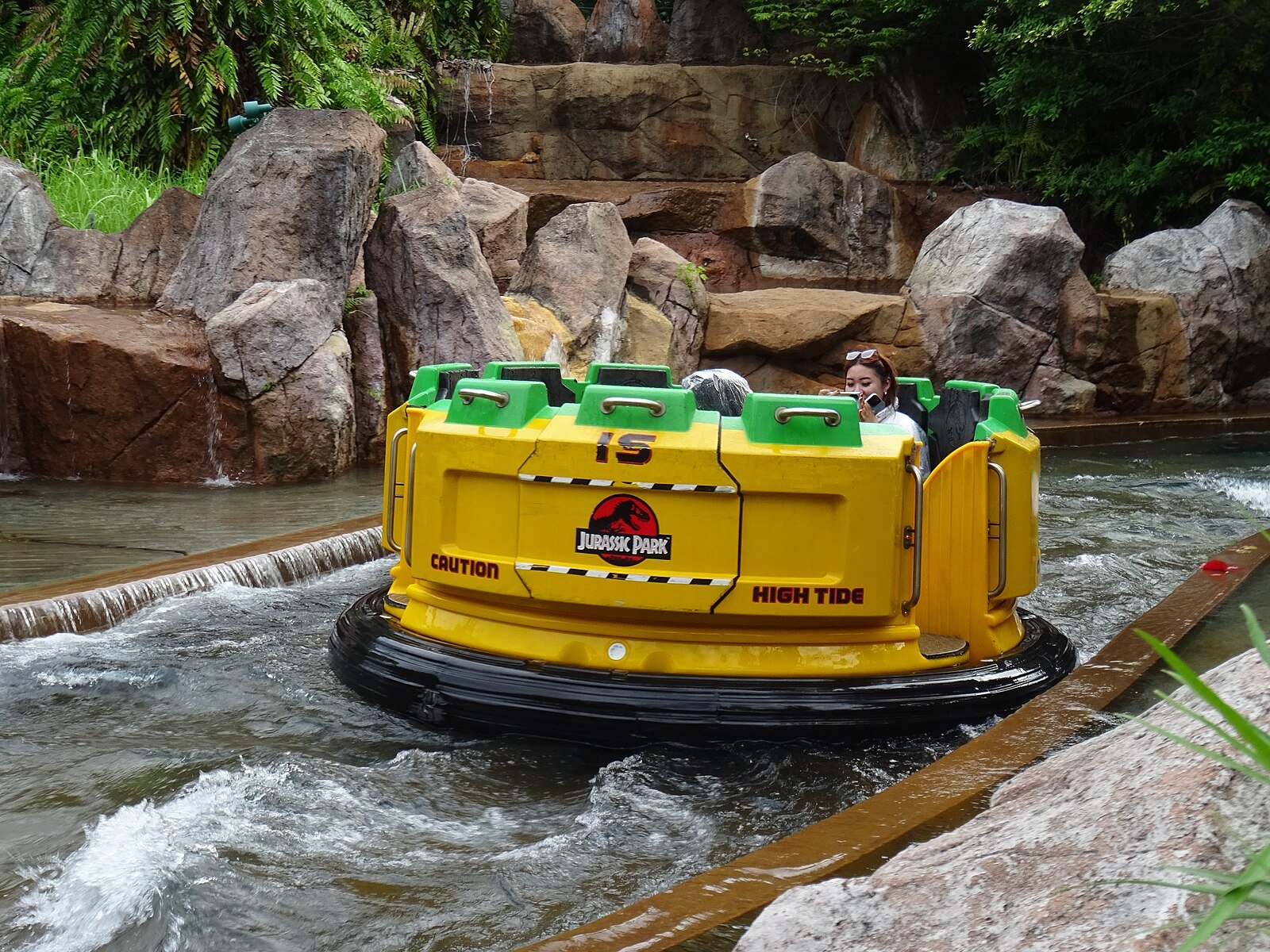 Thrilling water-based Jurassic Park ride featuring lush greenery, animatronic dinosaurs, and a splash drop, surrounded by immersive prehistoric-themed scenery with excited riders.