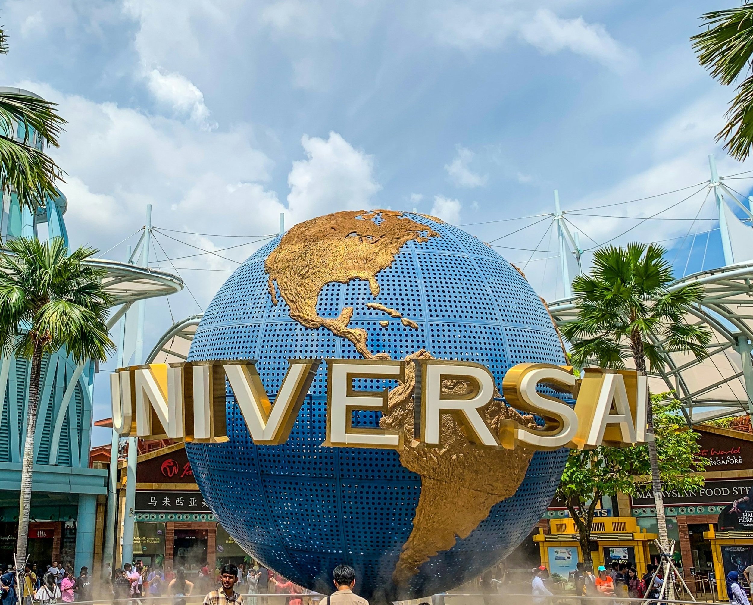 Colorful theme park entrance with iconic globe logo, lively crowds, and vibrant attractions under a bright sky. Exciting entertainment destination.