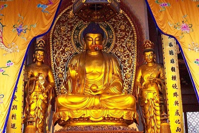 Close-up of a serene gold Buddhist statue at Lingyin Temple, surrounded by intricate cultural art and incense smoke.