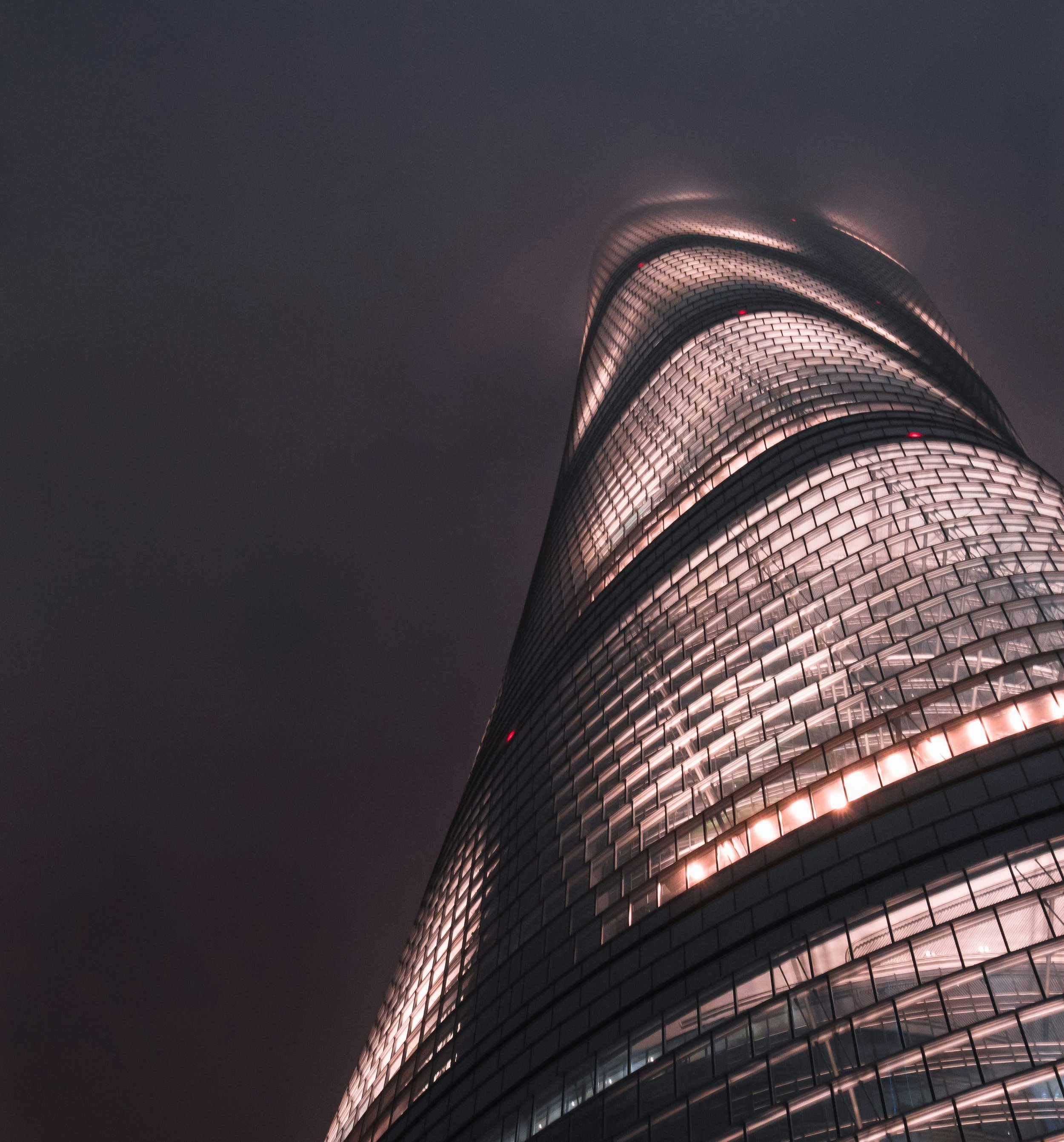 Low-angle shot of Shanghai Tower glowing at night, illustrating its sleek spiral design and sustainable architecture.