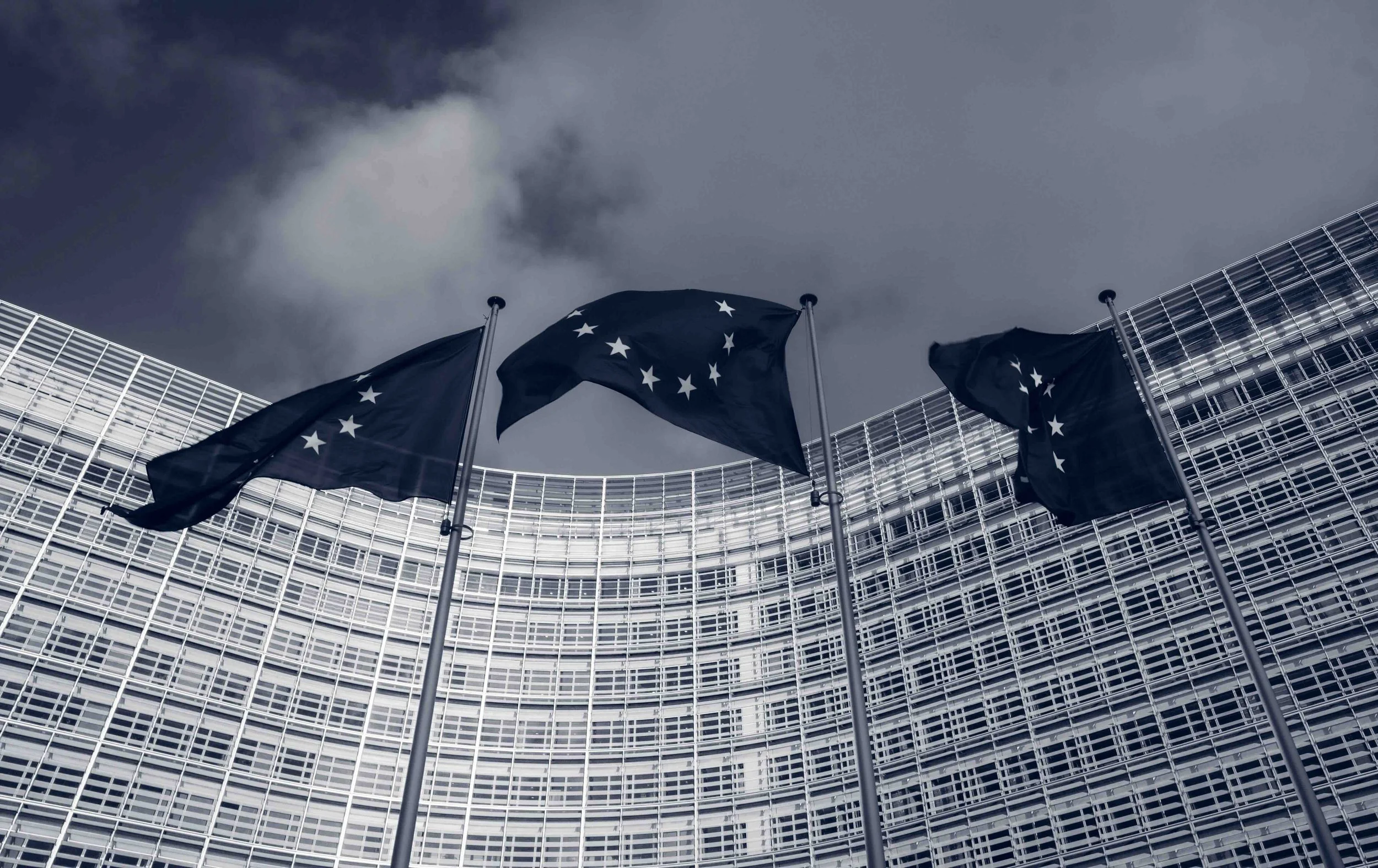 Brussels, Belgium | Low-angle view of European Union flags flying outside the Berlaymont building, headquarters of the European Commission.