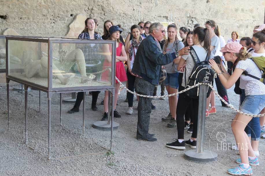 Students getting a tour of Pompeii by an acient history expert in front of a preserved body displayed in a glass case