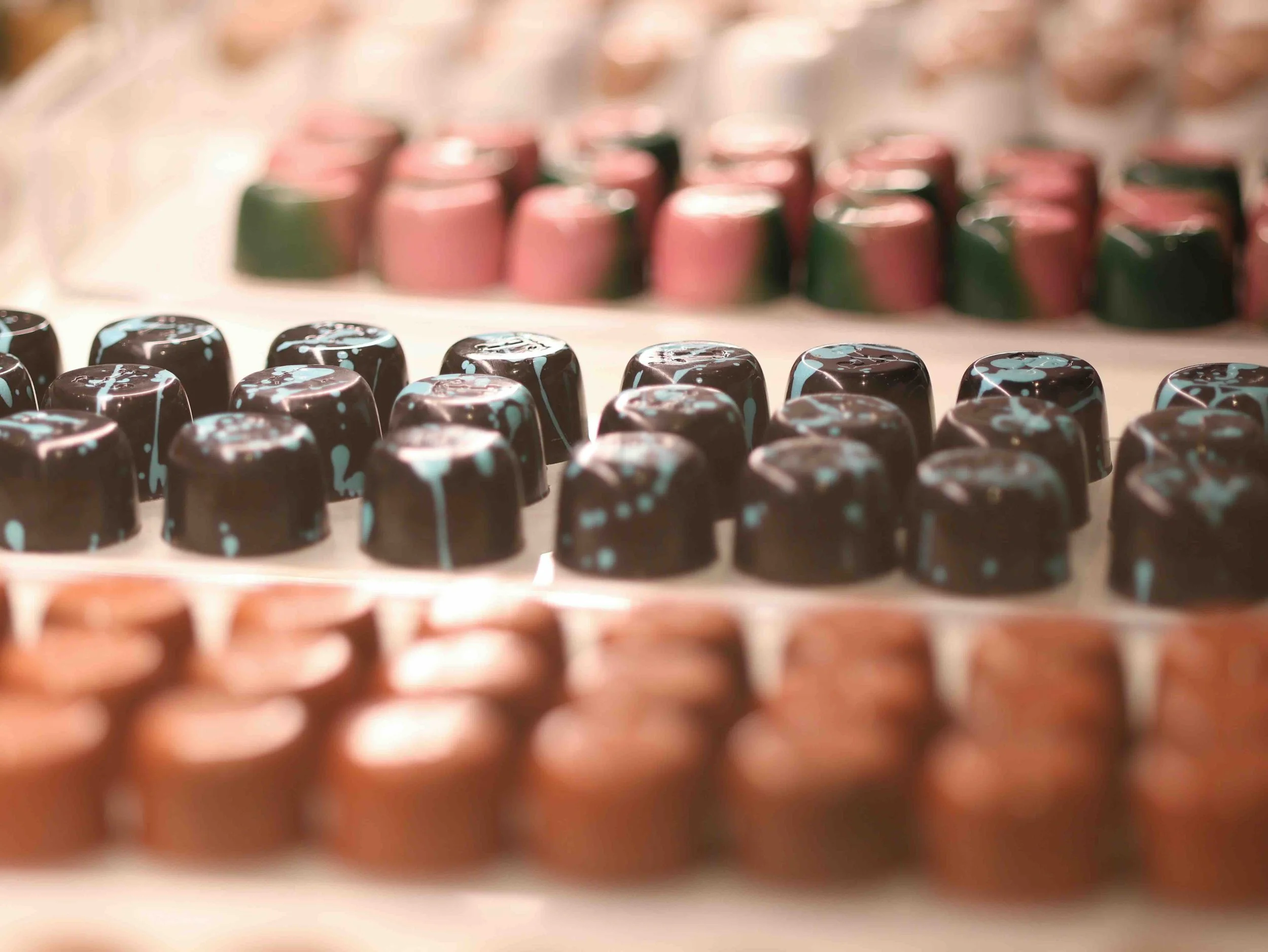 Brussels, Belgium | Rows of handmade Belgian chocolates and pralines in pink, green, dark chocolate with teal detailing, and milk chocolate varieties.