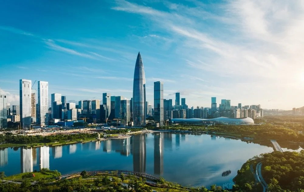 Shenzhen skyline by day, featuring the distinctive curved silhouette of a central skyscraper reflected in the waterfront below.