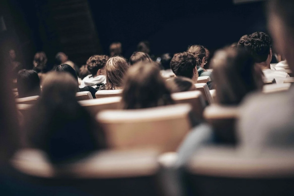 Students seated in a university lecture theatre, viewed from behind, focused on a presentation during a campus immersion session.