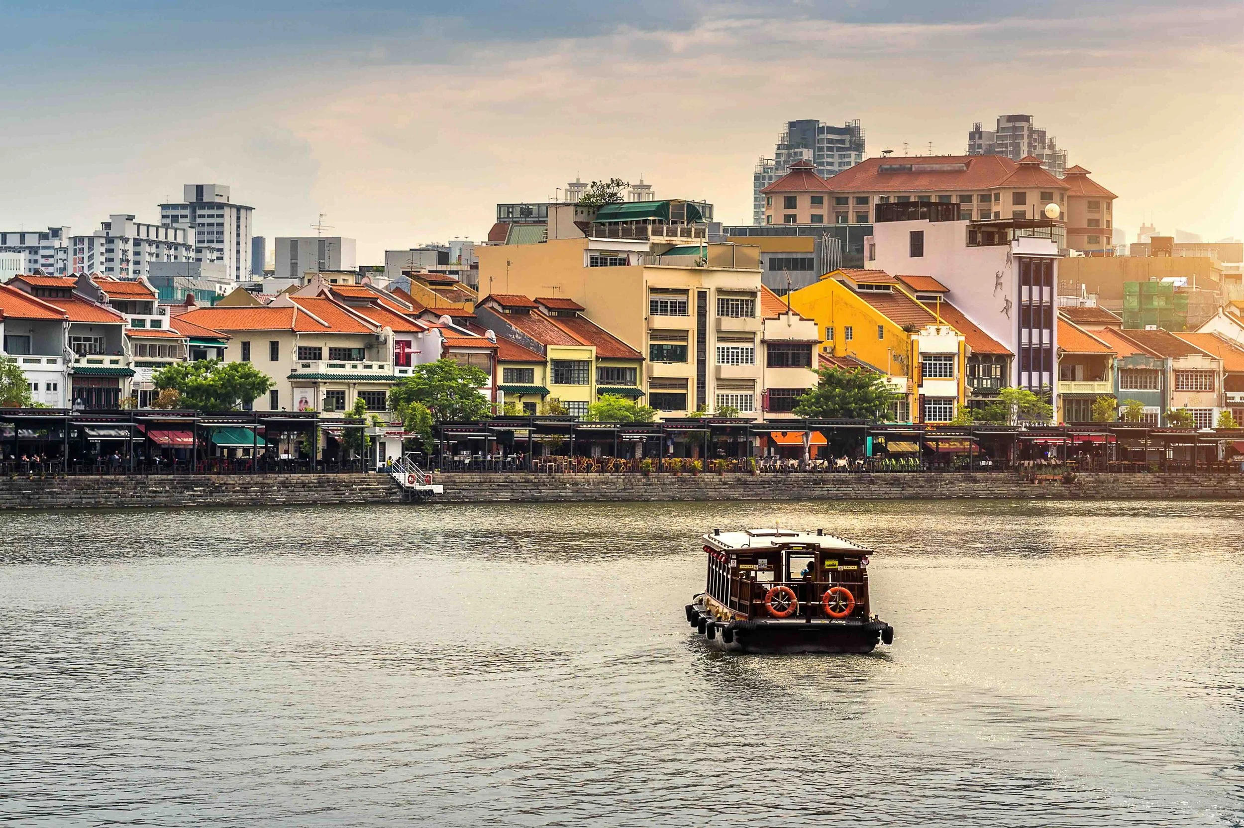 A traditional bumboat drifts past the restored shophouses of Boat Quay as the sun sets over the Singapore River — tracing the trade routes that shaped a global city.
