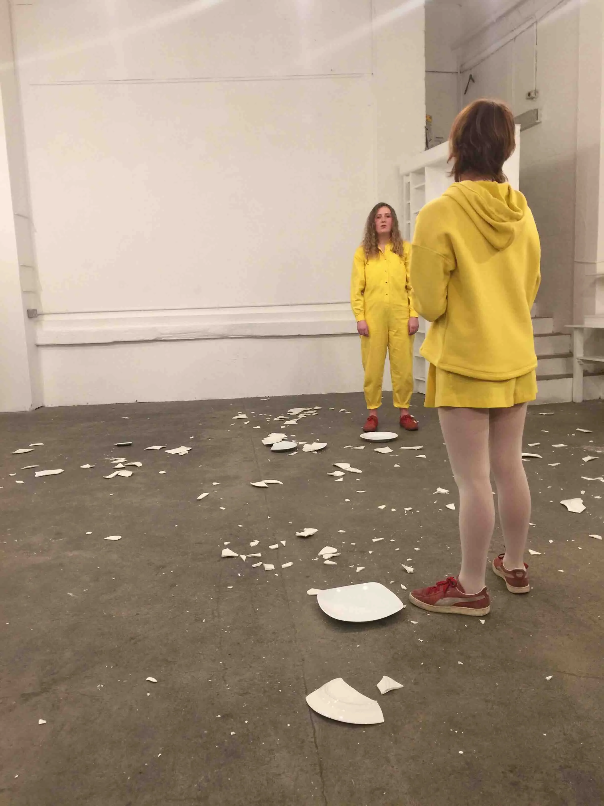 Two drama students in yellow costumes performing a devised theatre piece with broken crockery — the kind of bold, provocative performance workshop experienced on a Libertas Travel Performing Arts school tour.